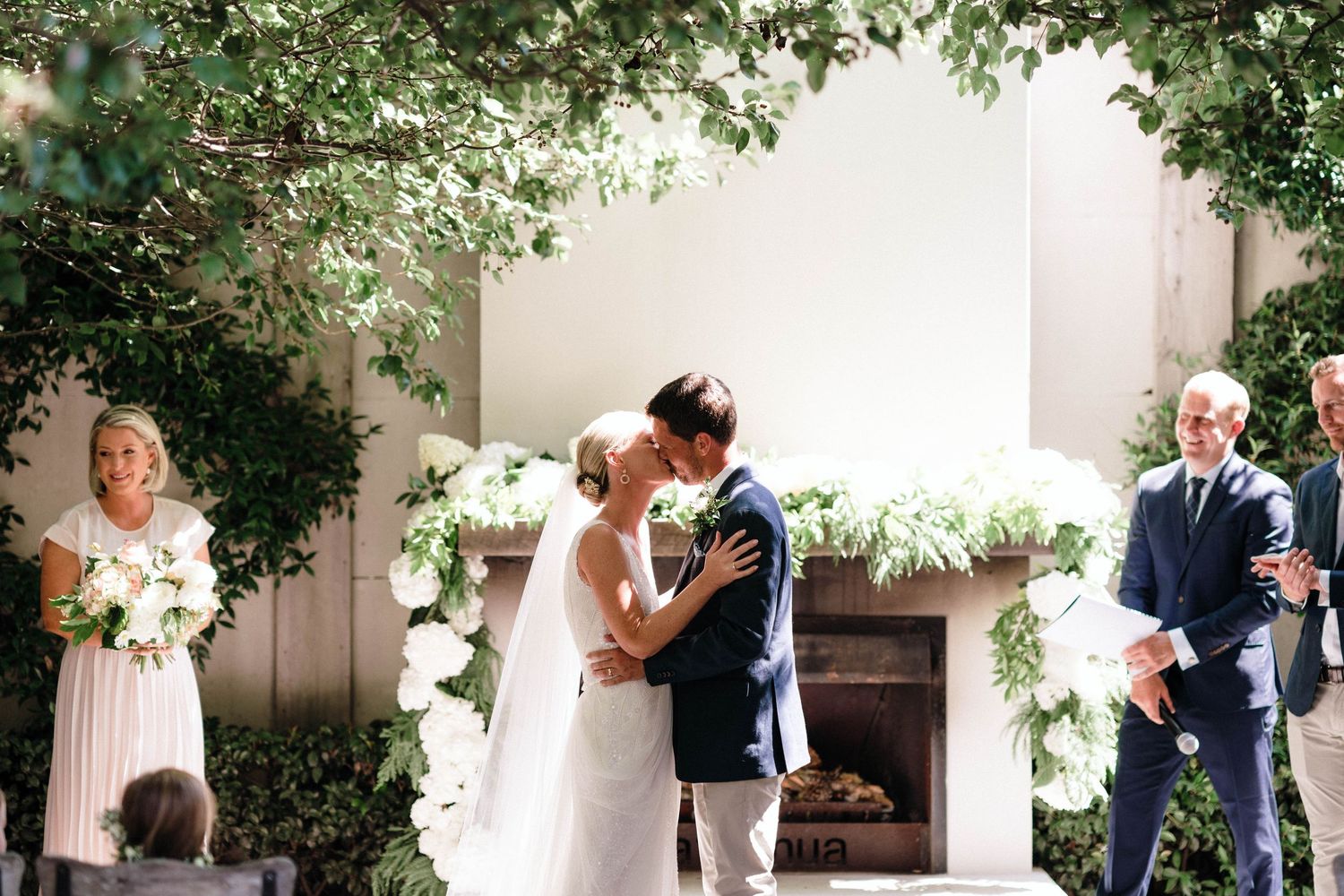 Intimate wedding moment at outdoor venue with white fireplace and climbing vines.