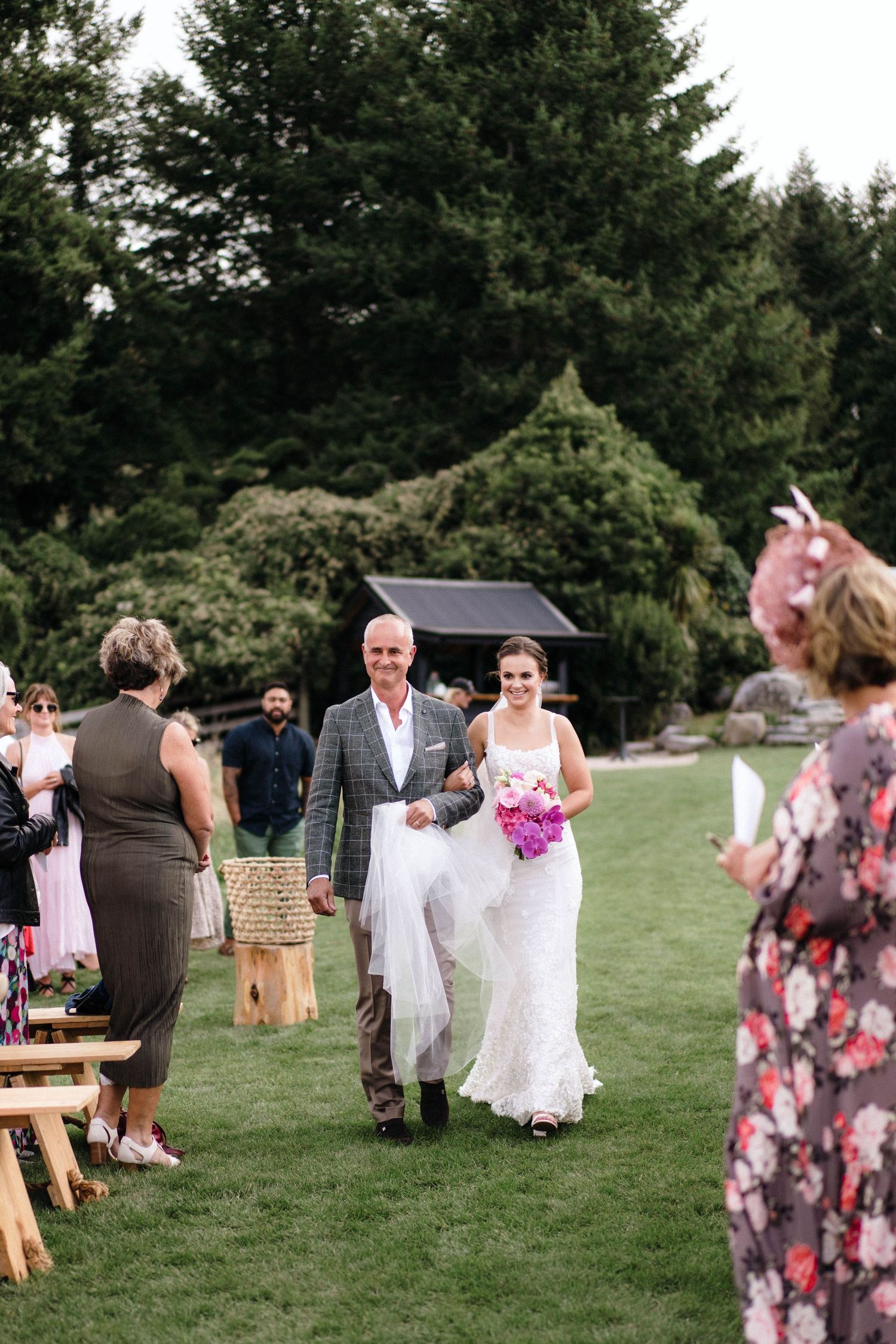 Outdoor wedding ceremony with rustic wooden benches and evergreen trees in the background.
