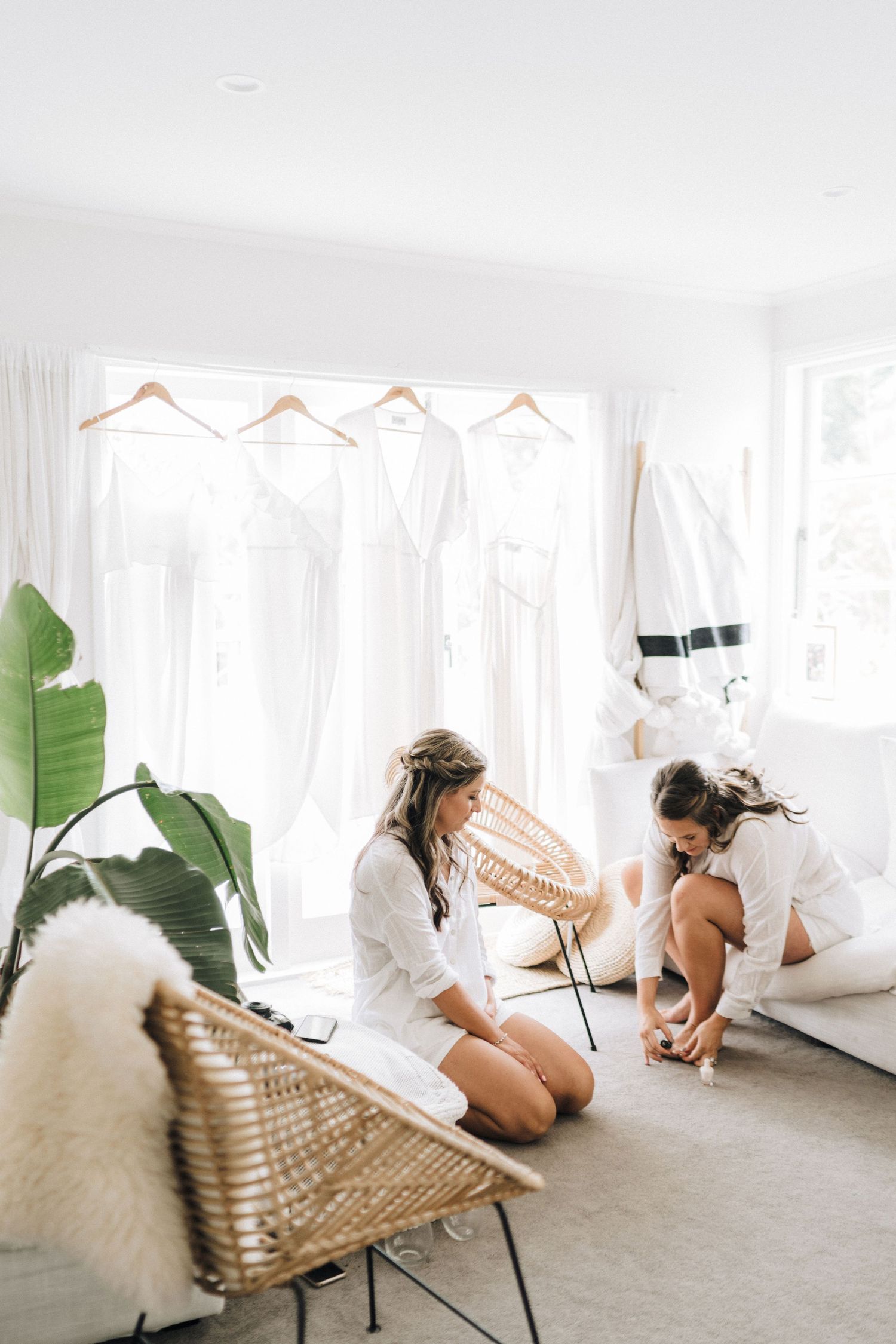 Two people in white robes getting ready in a bright minimalist room with hanging white dresses.