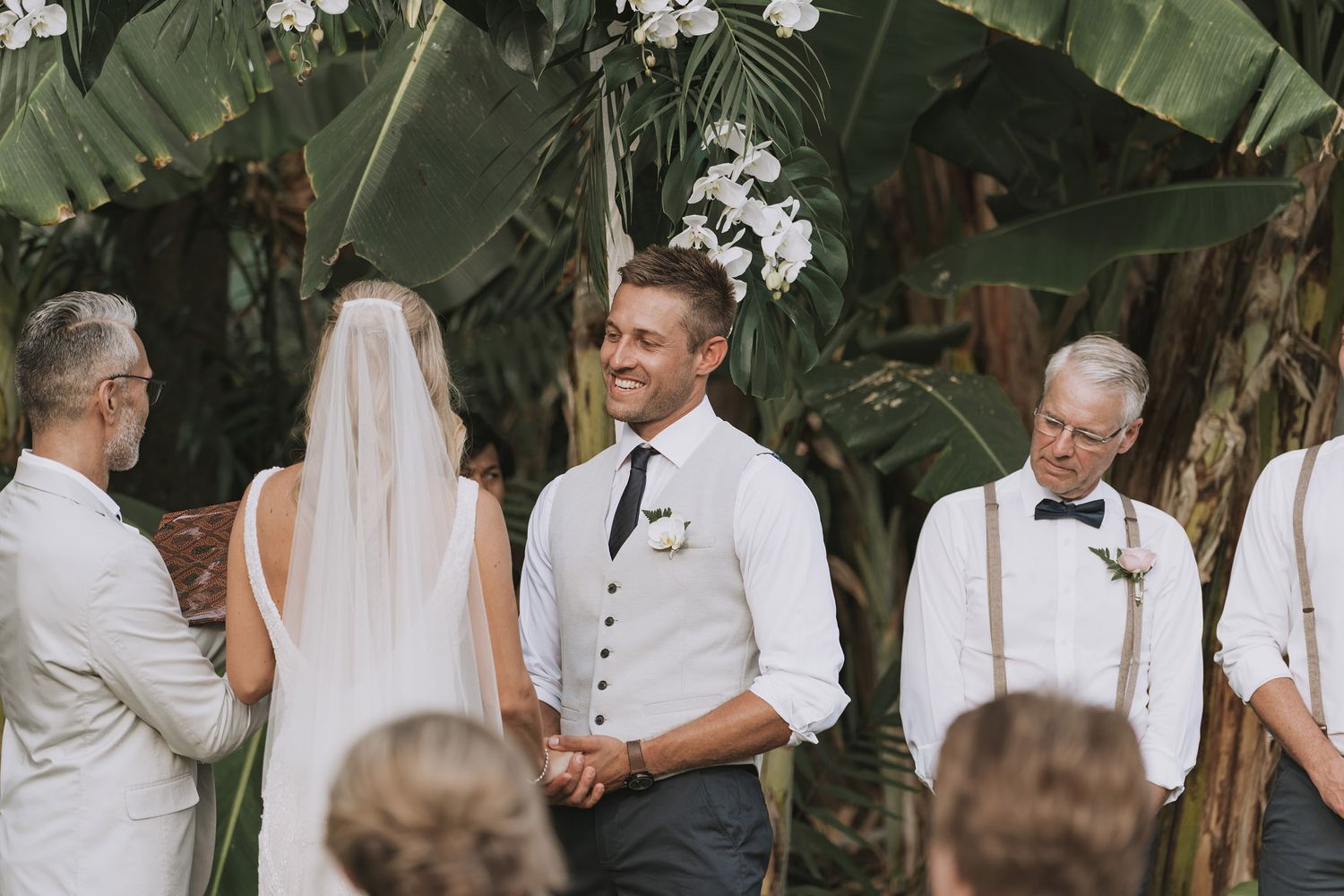 Wedding couple shares intimate moments in a lush tropical garden setting with white floral arrangements.