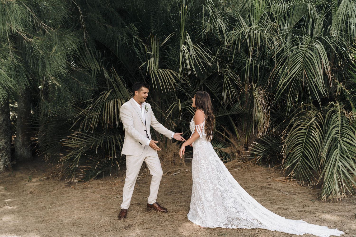 Couple in wedding attire posing together against tropical palm background.