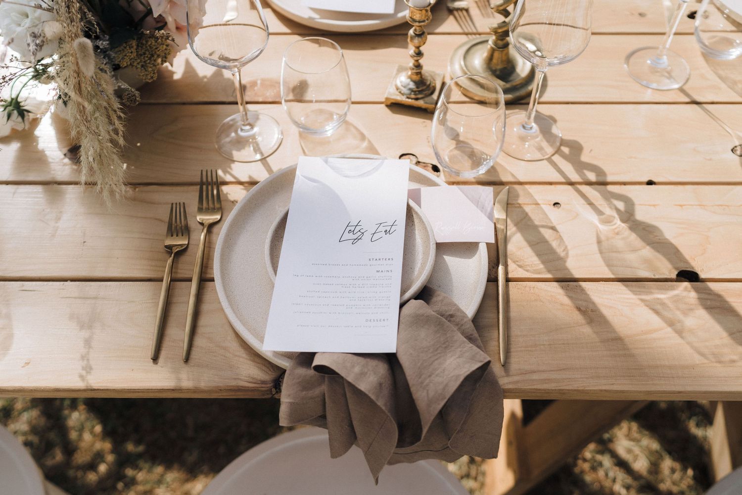 Rustic wedding table setting with place cards and elegant tableware on wooden surface.