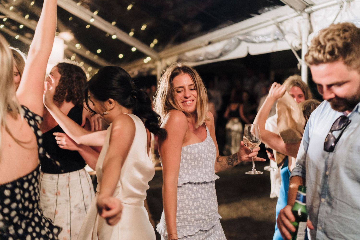 Wedding party dancing and celebrating at nighttime reception with string lights overhead.