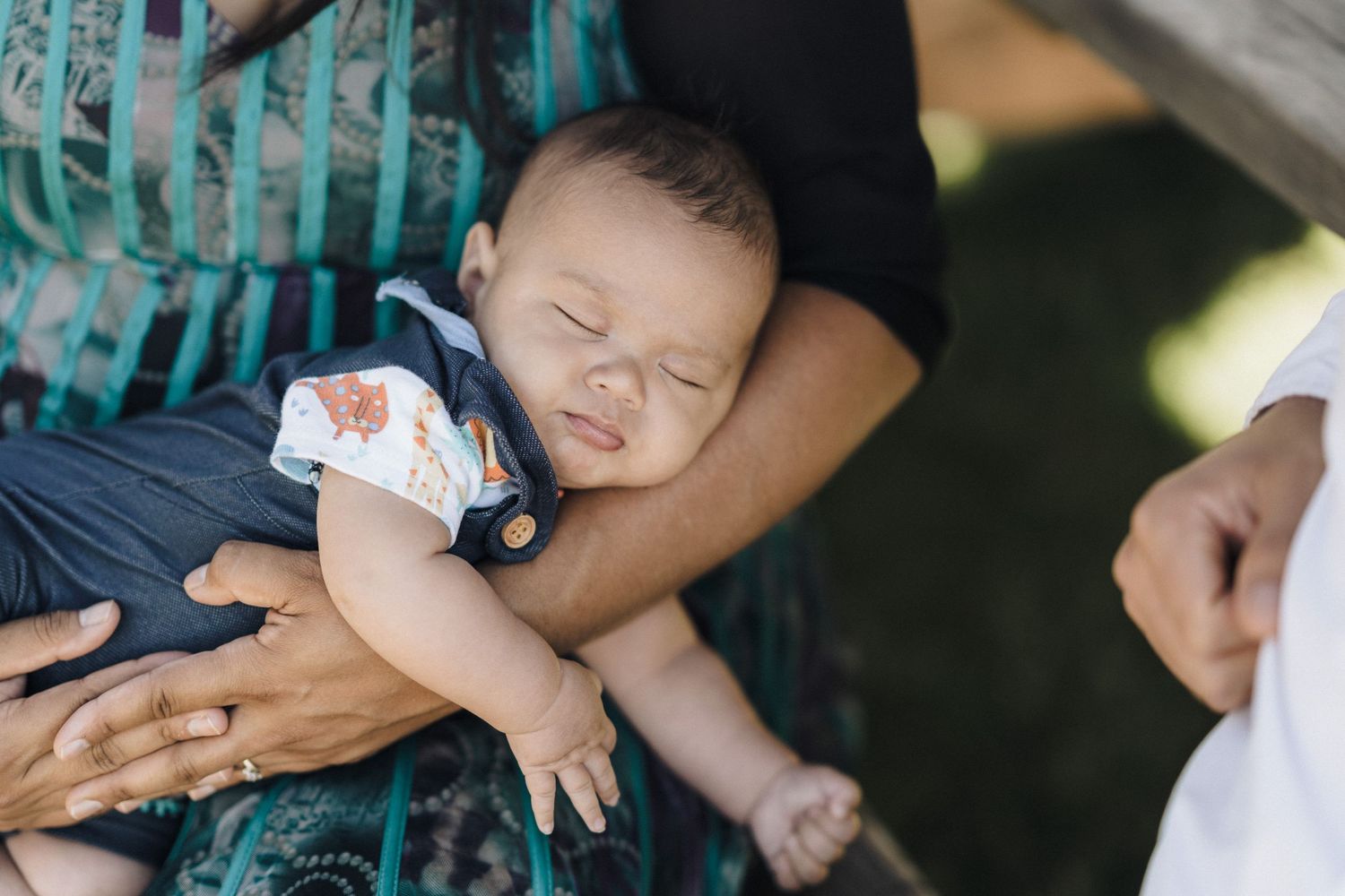 Sleeping baby in formal wear being cradled during outdoor event.