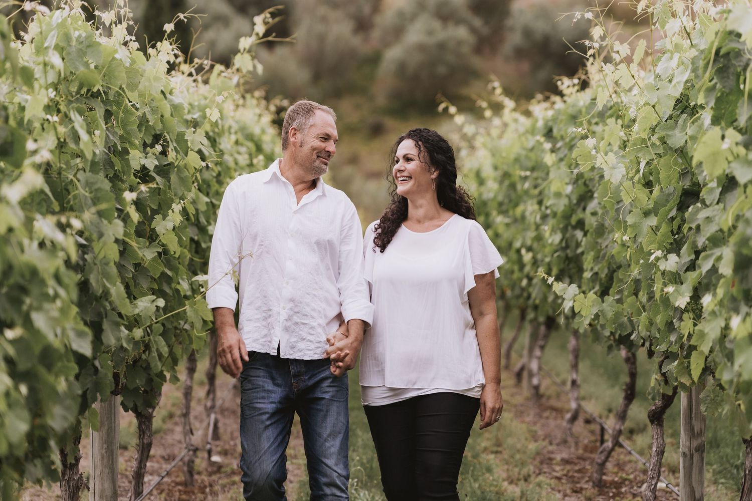 A couple walks together through a lush vineyard during a romantic outdoor photoshoot with sunlit grapevines.