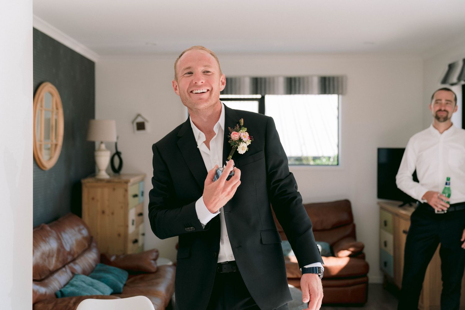 A joyful moment at a wedding shows someone in a black suit smiling and gesturing expressively in a living room setting.