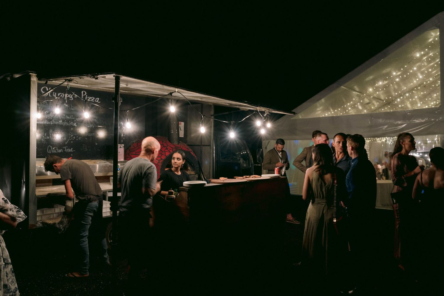 Dark outdoor wedding reception tent illuminated with string lights creating a romantic ambiance.