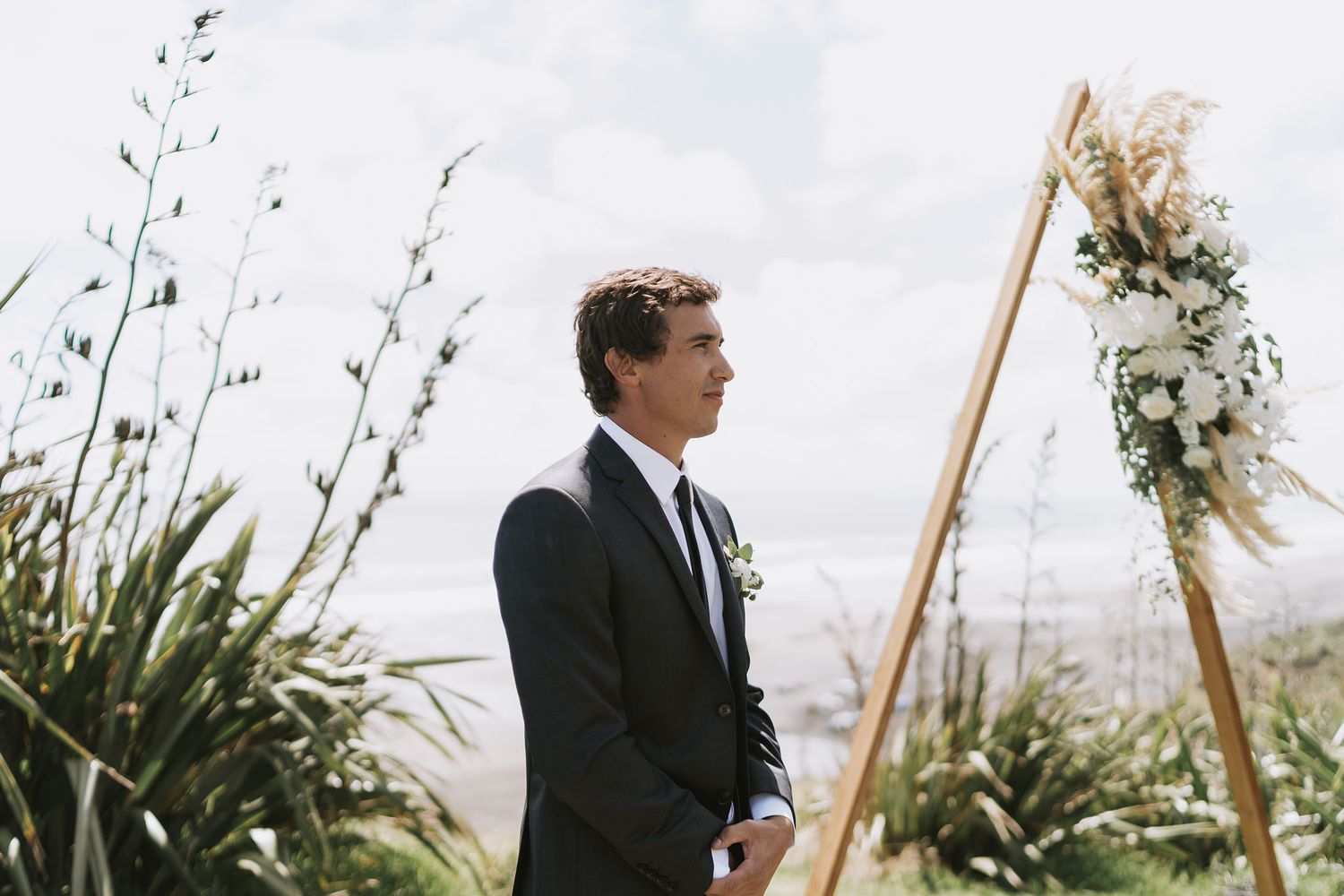 A person in a dark suit and tie stands outside with bamboo poles swaying in a gentle breeze.