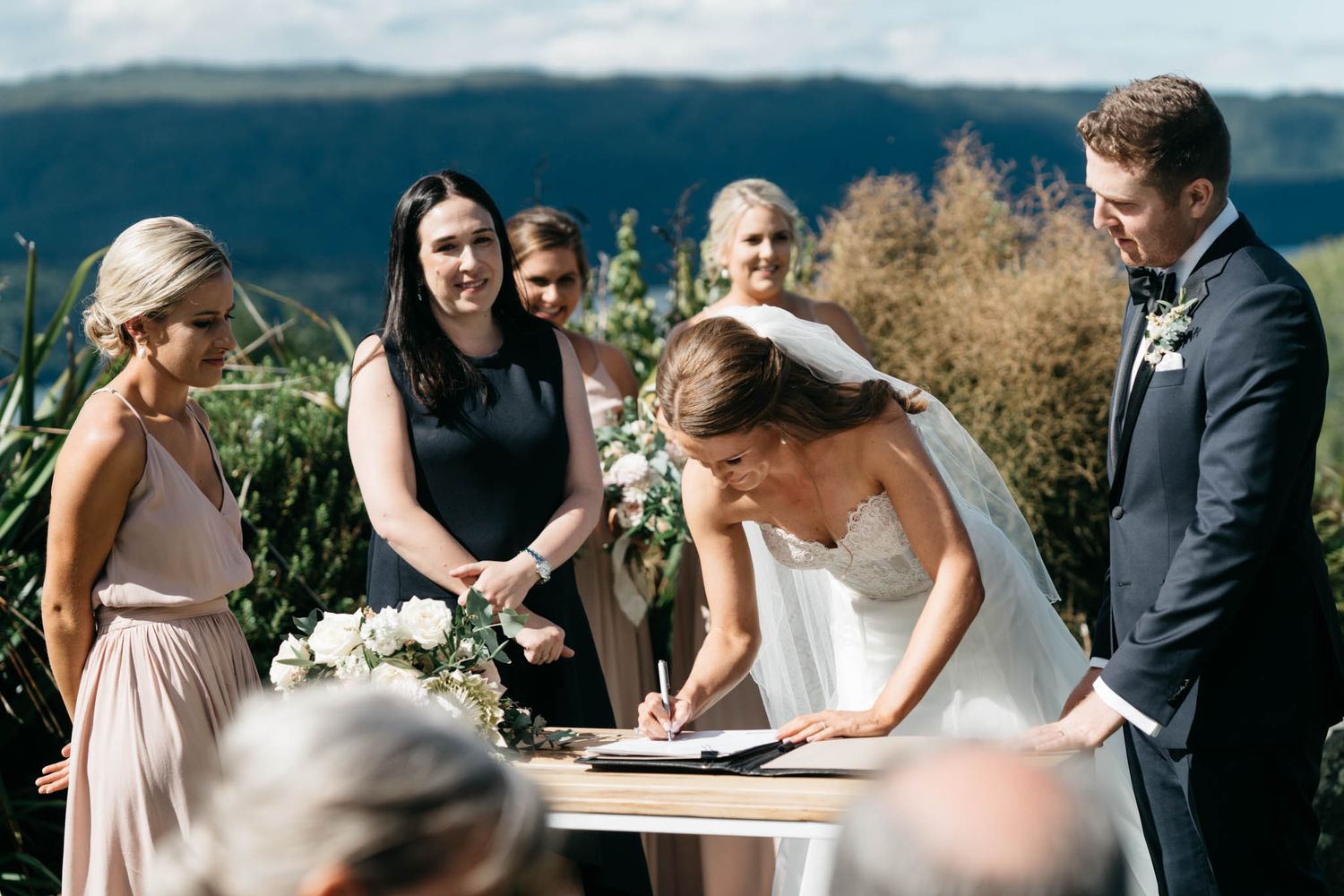 Elegant outdoor mountain wedding ceremony signing documents with scenic natural backdrop framed by floral arrangements.