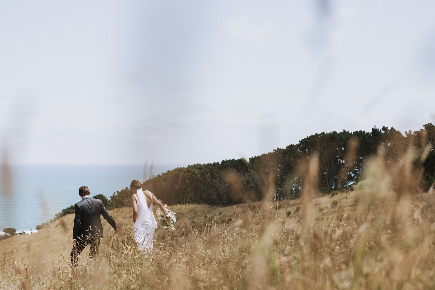 Two people walking together through golden grass on a hilltop against a mountain backdrop on a misty day.