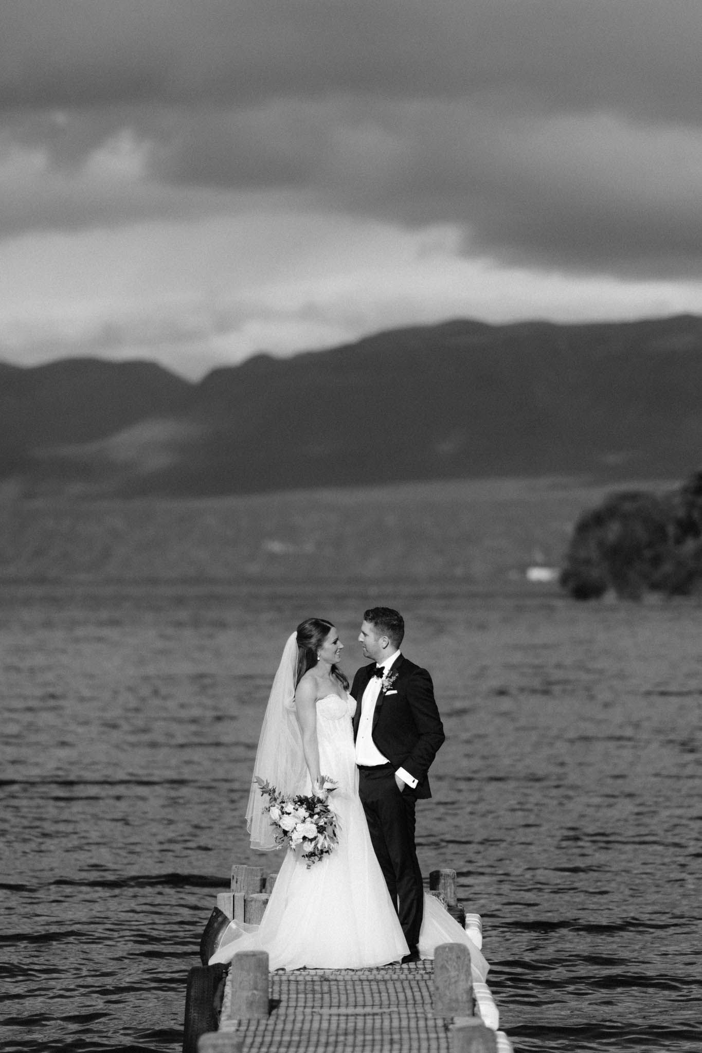 A couple shares a romantic moment on a dock overlooking a misty lake with mountains in the background.