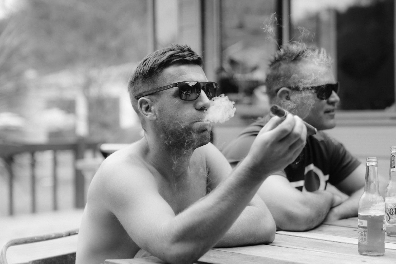 Two people in sunglasses sitting at an outdoor table with drinks on a sunny day in black and white.
