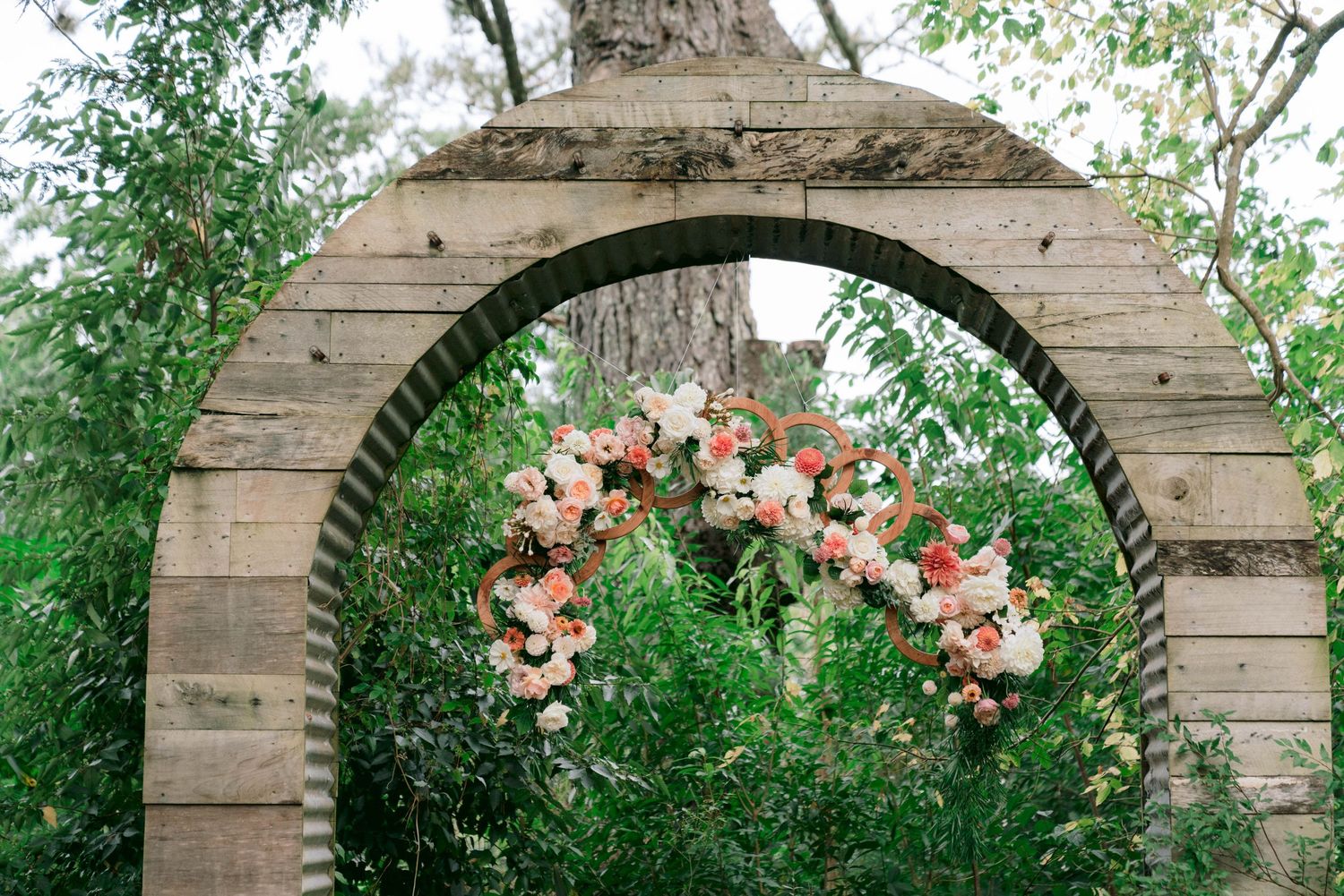 Rustic wooden arch decorated with peach and pink flowers for outdoor wedding ceremony.