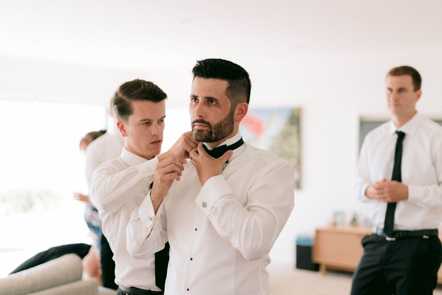 People in formal white shirts and ties getting dressed and making final adjustments indoors.