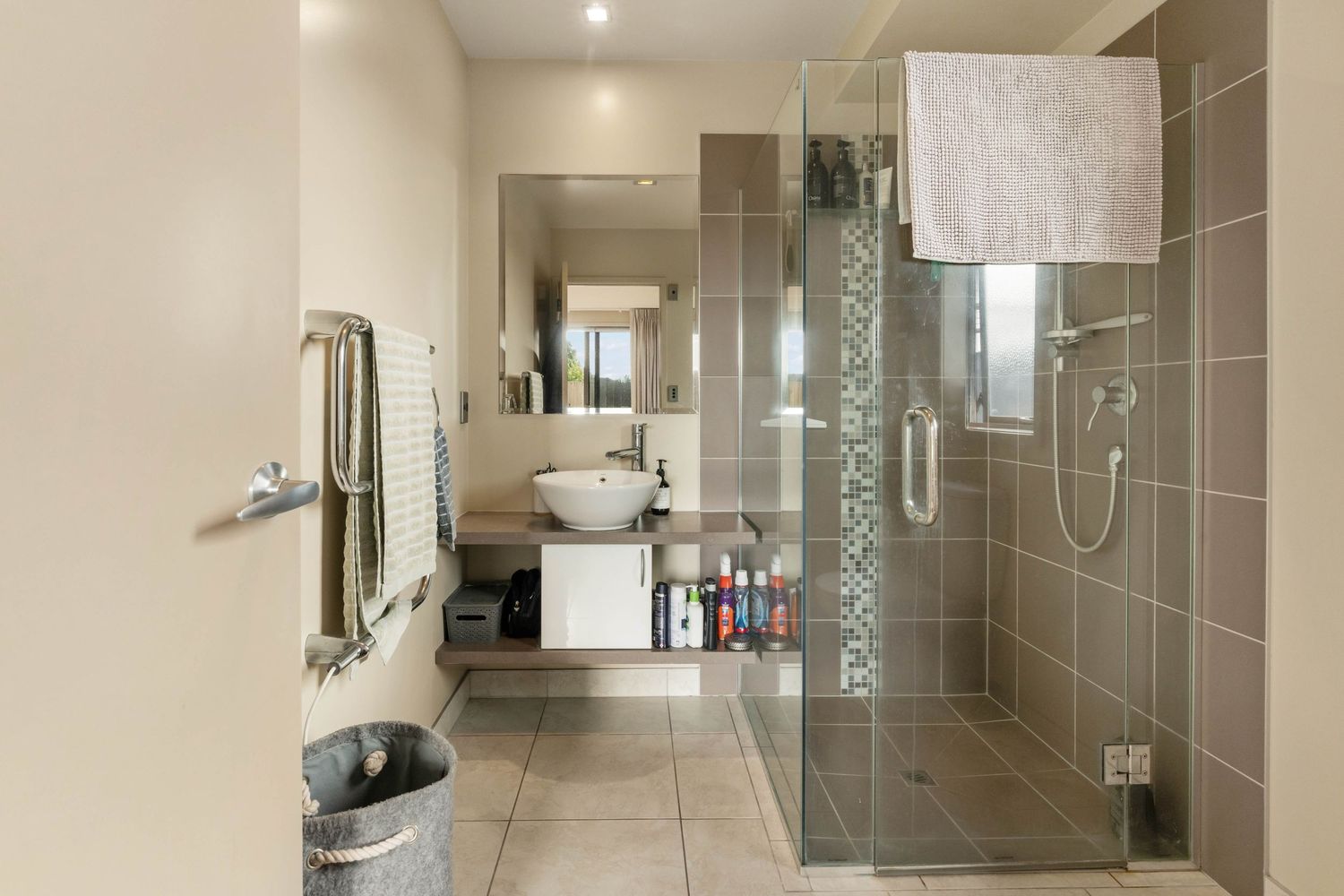 Modern bathroom interior with glass shower enclosure, gray tile walls, and chrome fixtures in neutral tones.