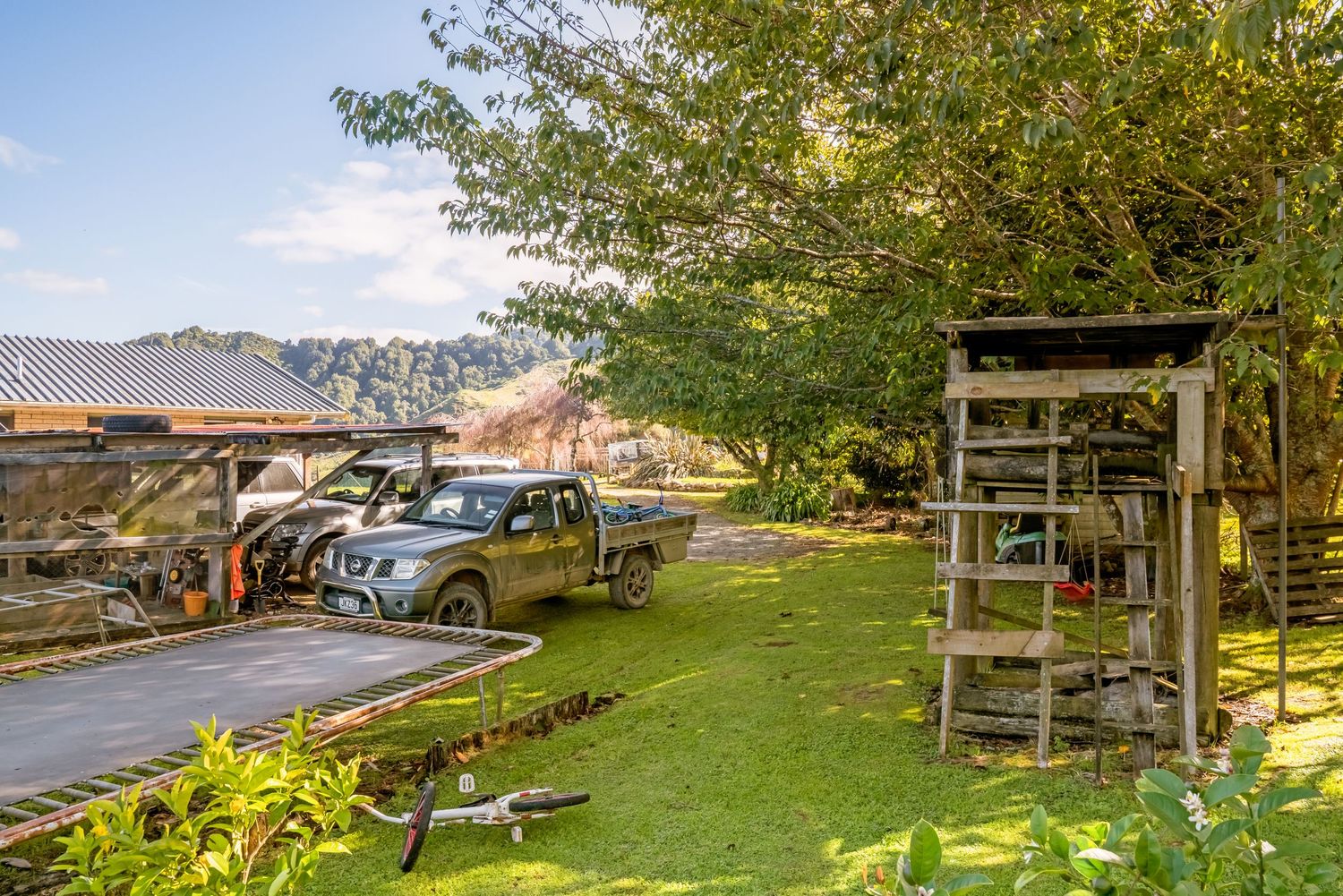 Farm entrance with parked cars and wooden structure next to a grassy area in a rural setting.