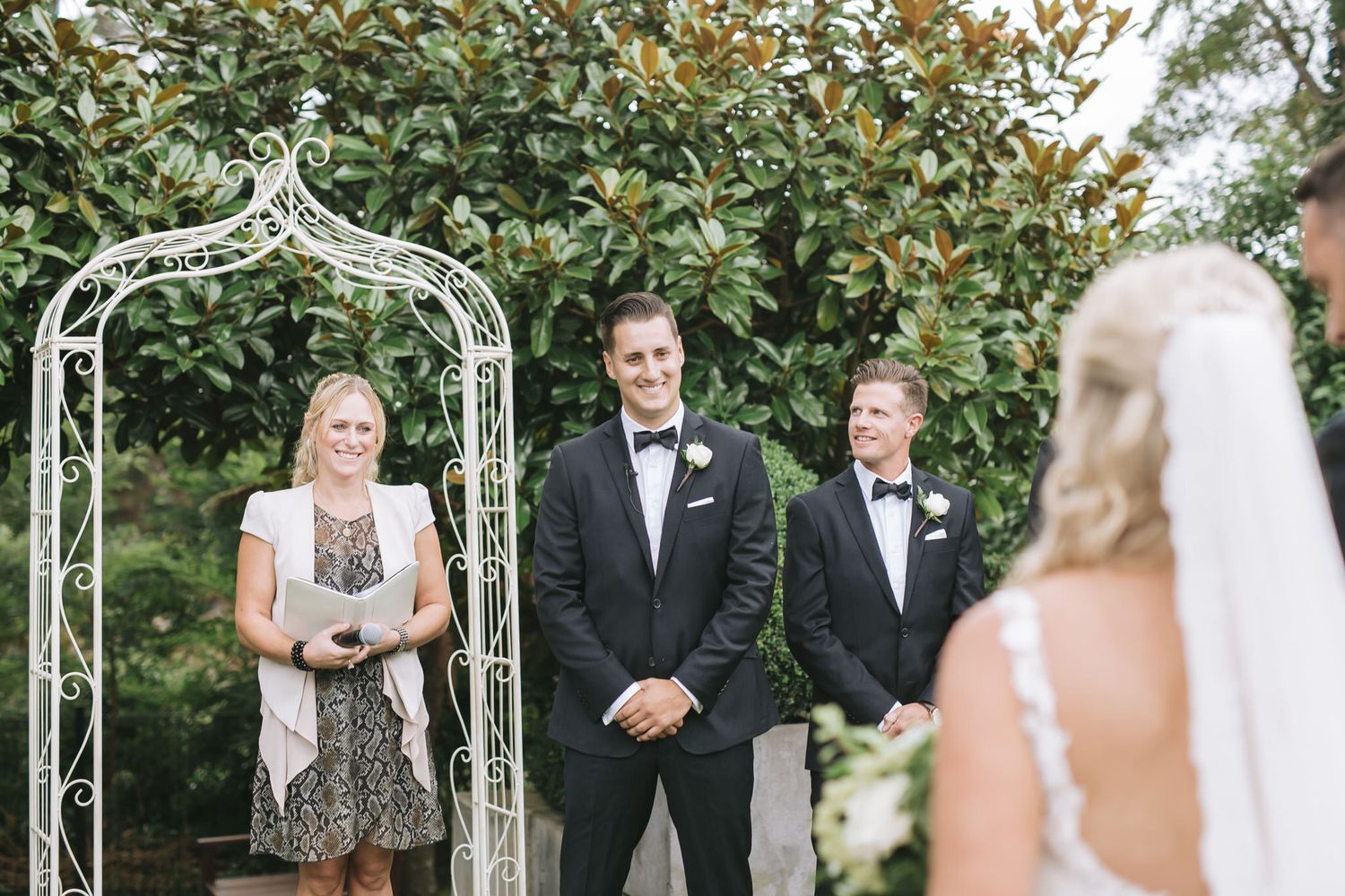 Outdoor wedding ceremony scene with an elegant white arbor and lush greenery in a garden setting.