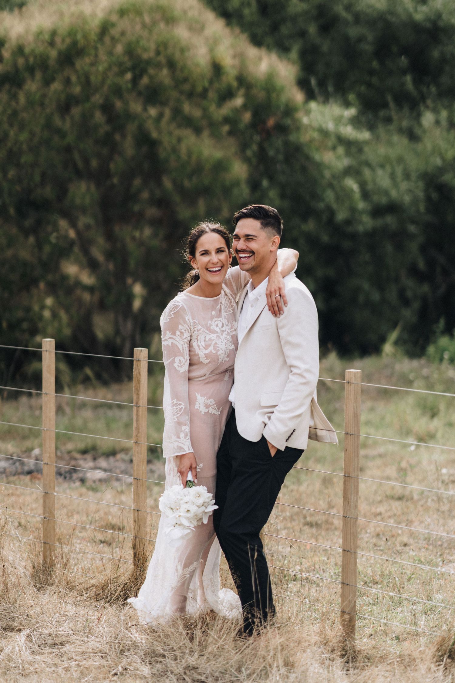 Joyful couple sharing laughter in a rustic outdoor setting with wooden fence posts.