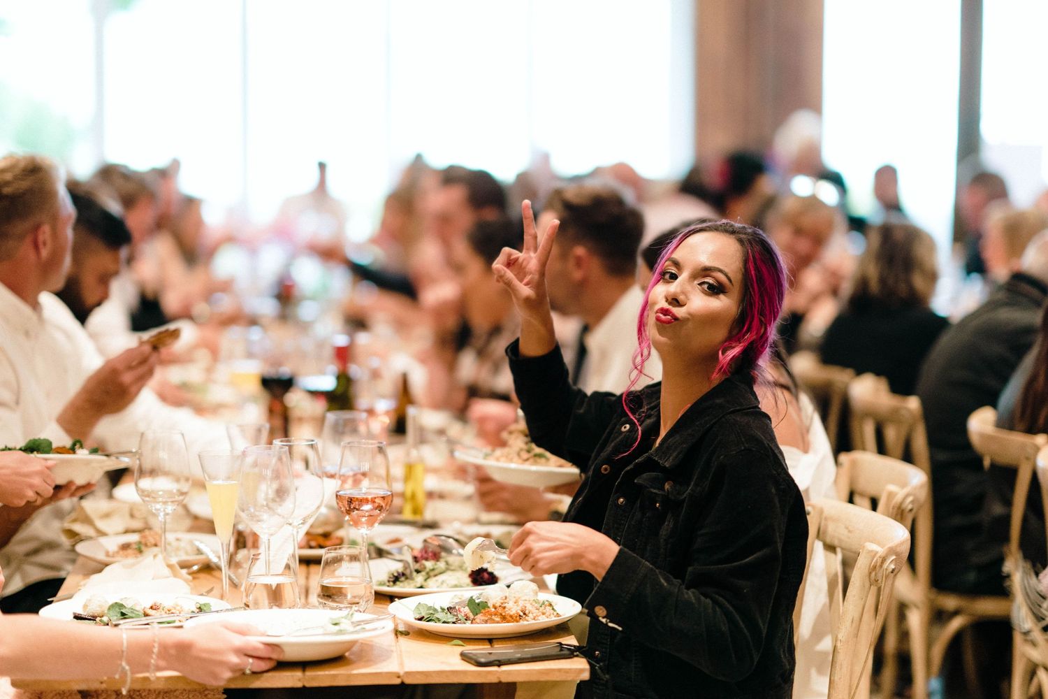 Wedding guests enjoy dinner and conversation at elegant tables in a wood-paneled reception space.