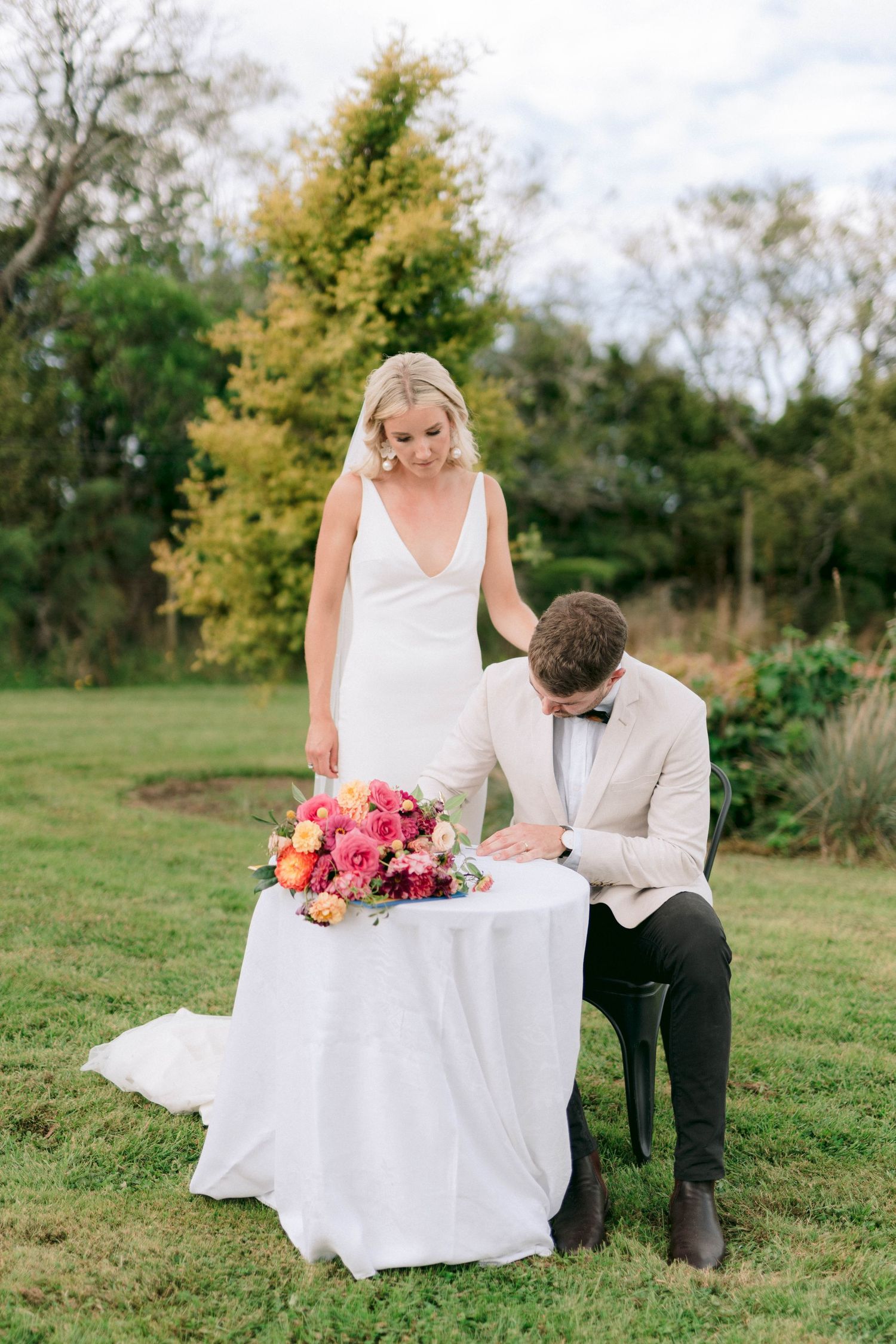 Couple signs marriage certificate outdoors with vibrant pink and coral bouquet on table.