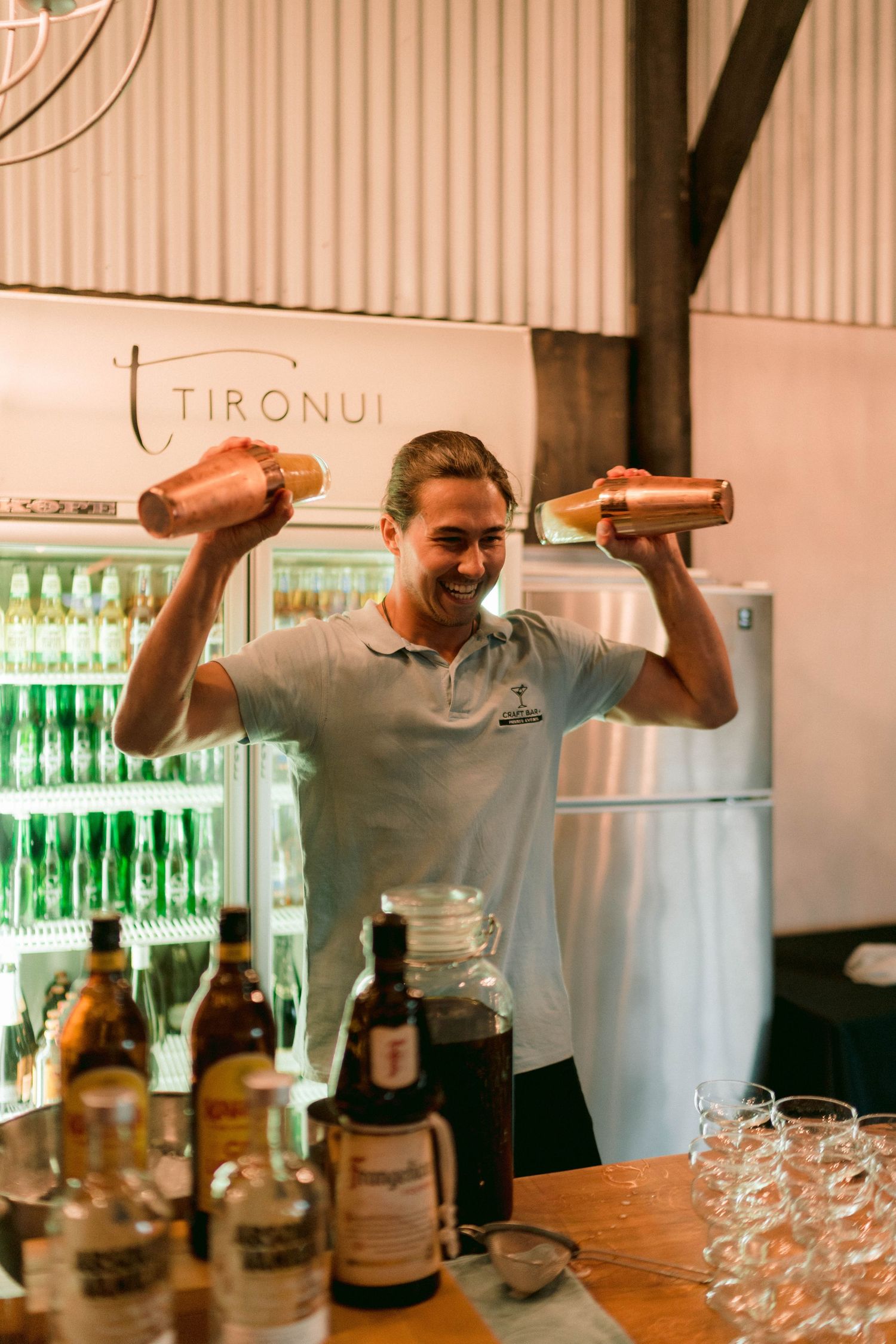 Bartender holding up bottles at wedding reception bar with drinks display.