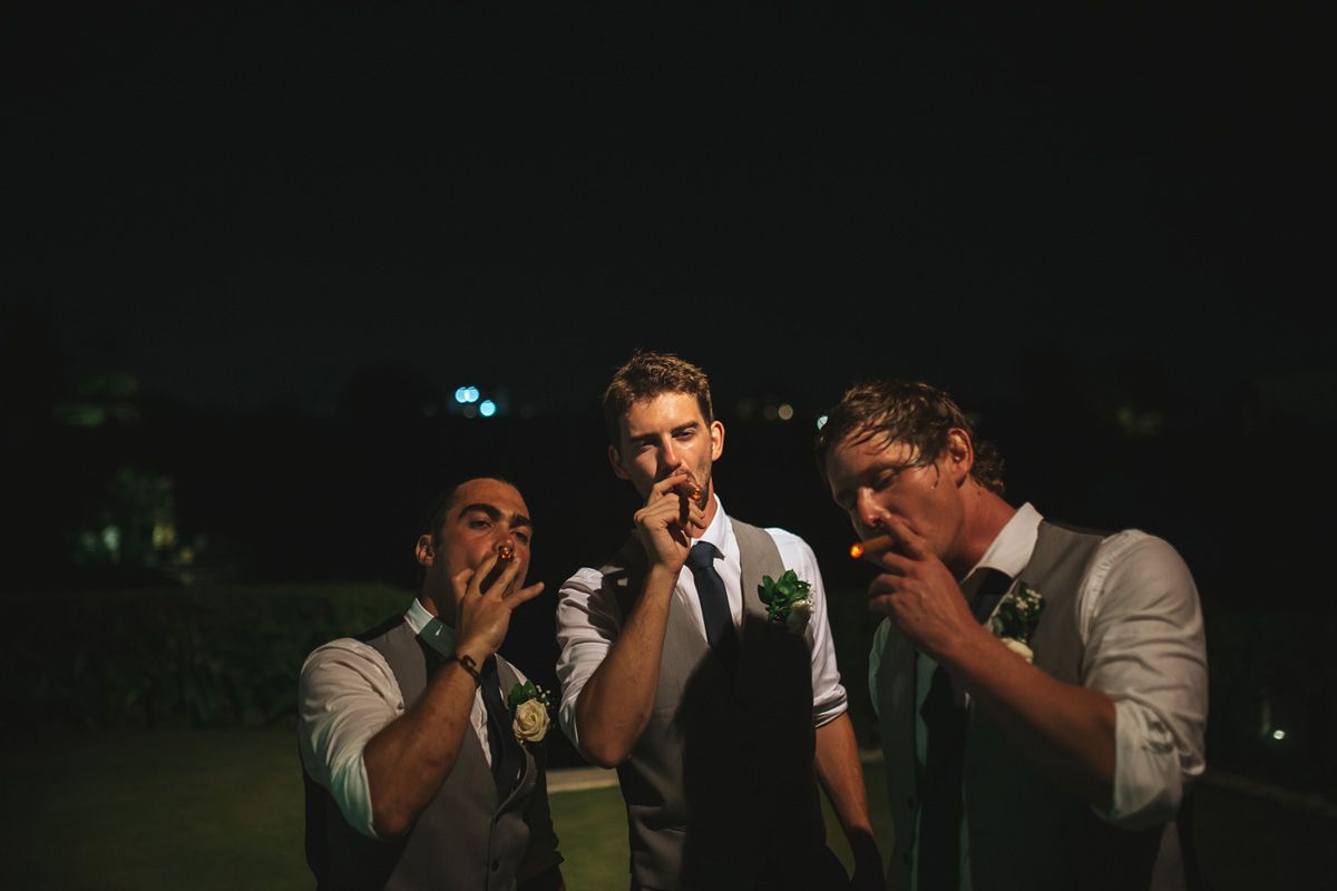 A group of friends celebrate at a wedding reception with enthusiastic cheering and dancing motions in low light.