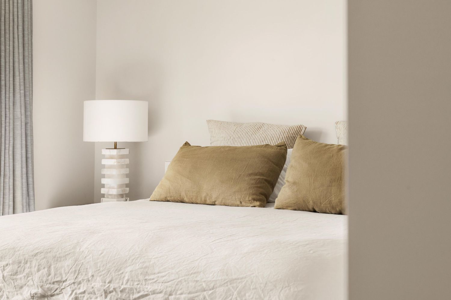 Serene bedroom with neutral tones, plush pillows, and natural light streaming through windows.