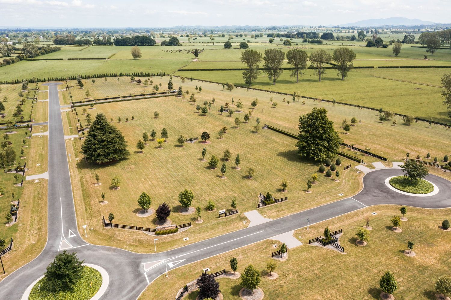 Aerial view of a rural roundabout intersection with newly planted trees in a pastoral landscape.