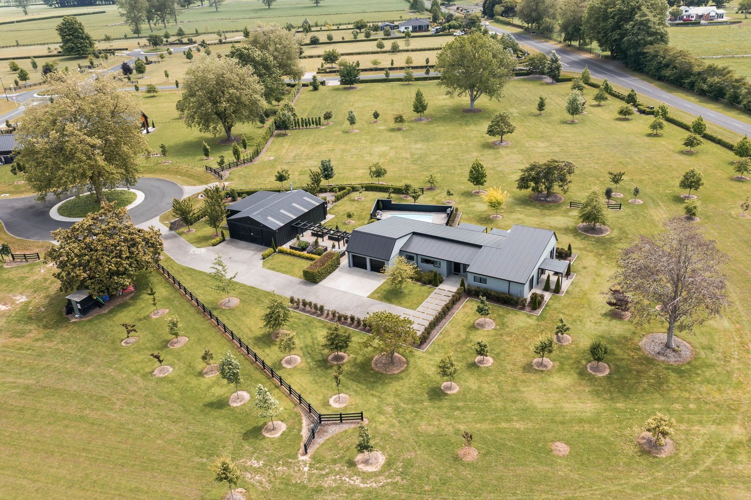 Aerial view of a modern rural property with multiple buildings and landscaped gardens surrounded by sprawling pastures.