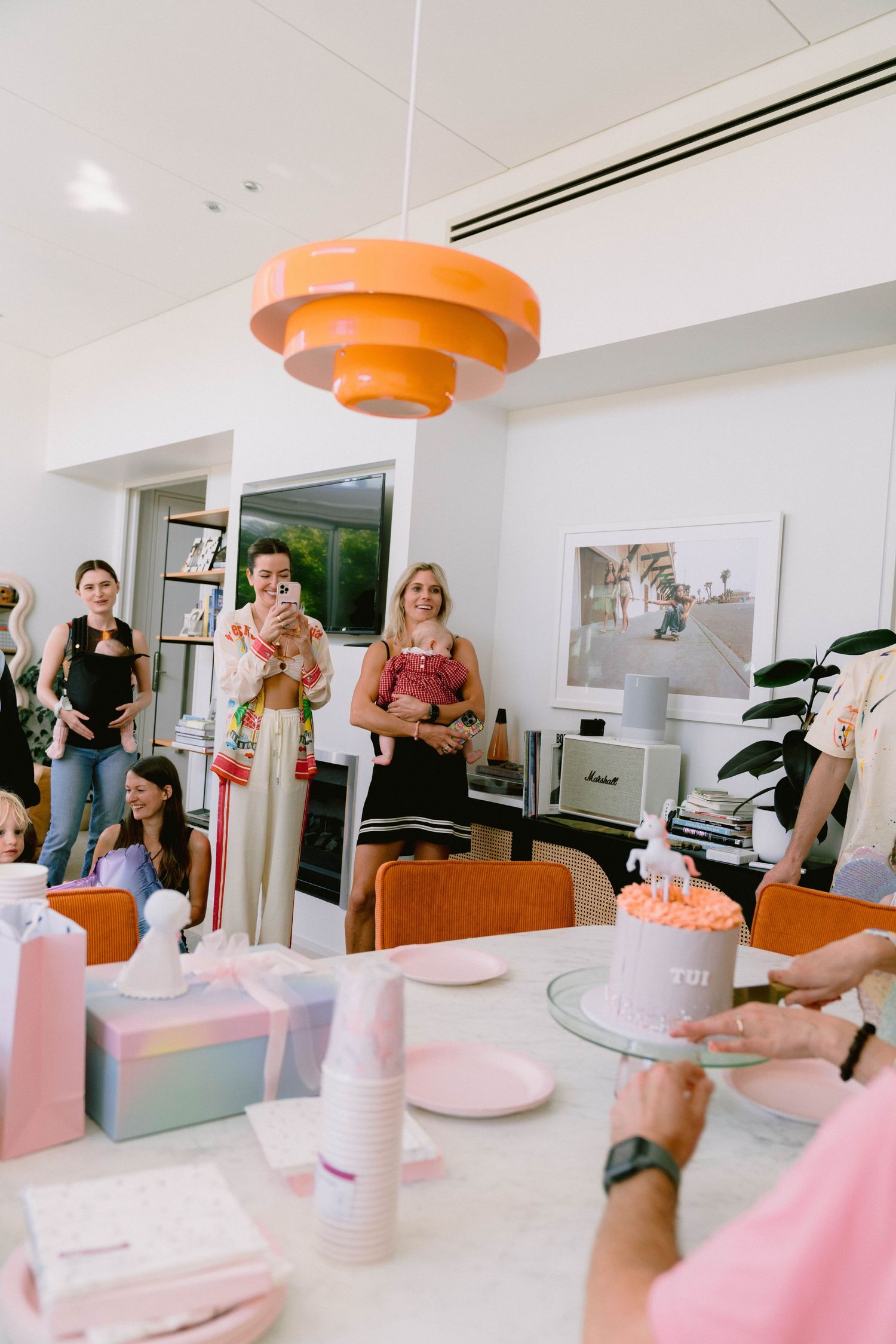 Modern interior party setup with pink and orange decorations and birthday cake on display.