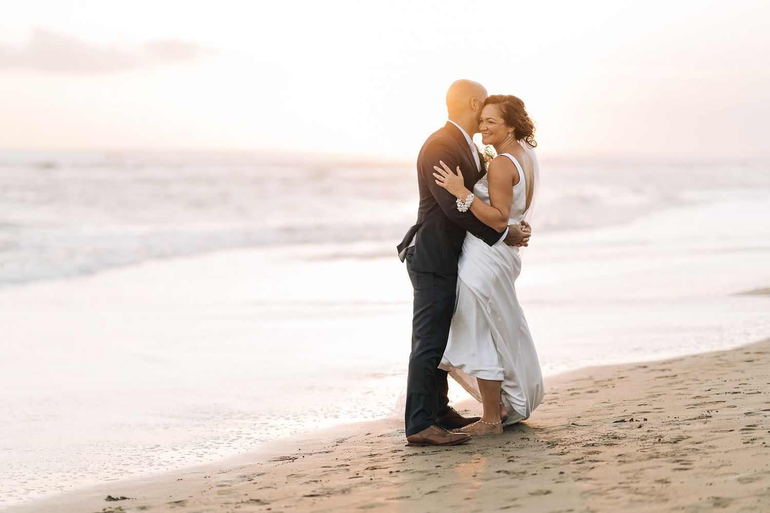 Romantic beach photoshoot with couples posing in elegant attire along the shoreline.