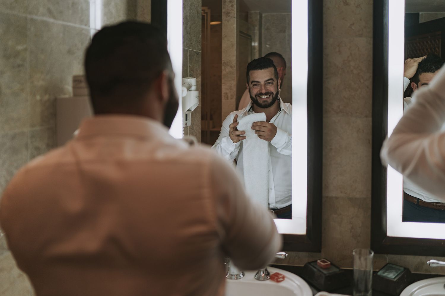 Person smiling in mirror while getting ready for formal event in white dress shirt.