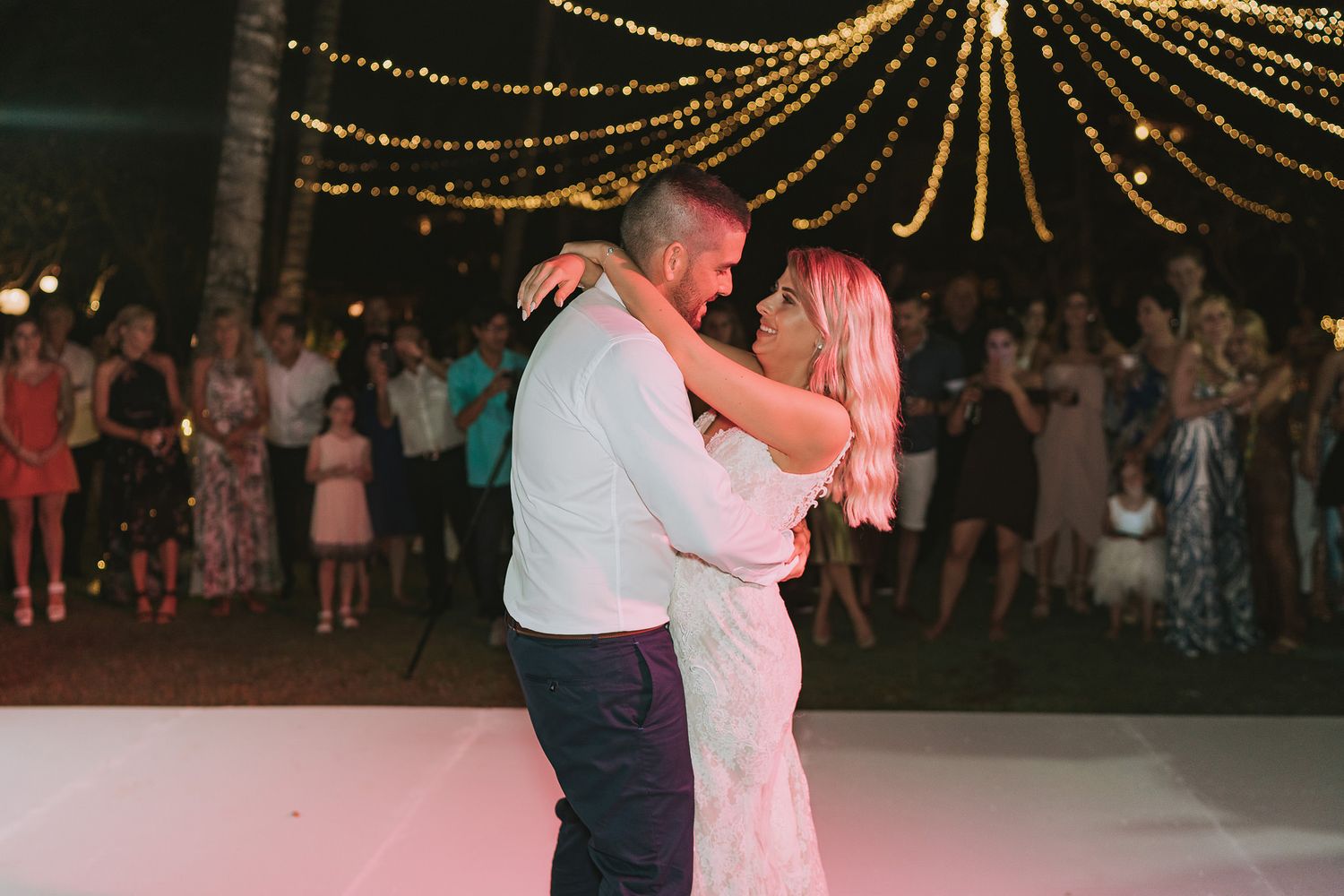 A couple shares their first dance under romantic string lights at their outdoor wedding reception.