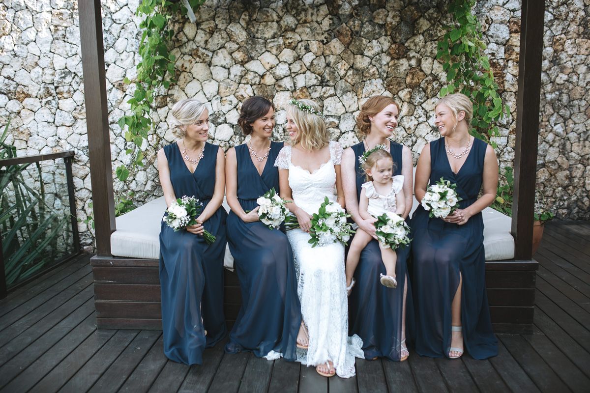 Wedding party in blue and white attire gathers for outdoor photos in front of floral decor.