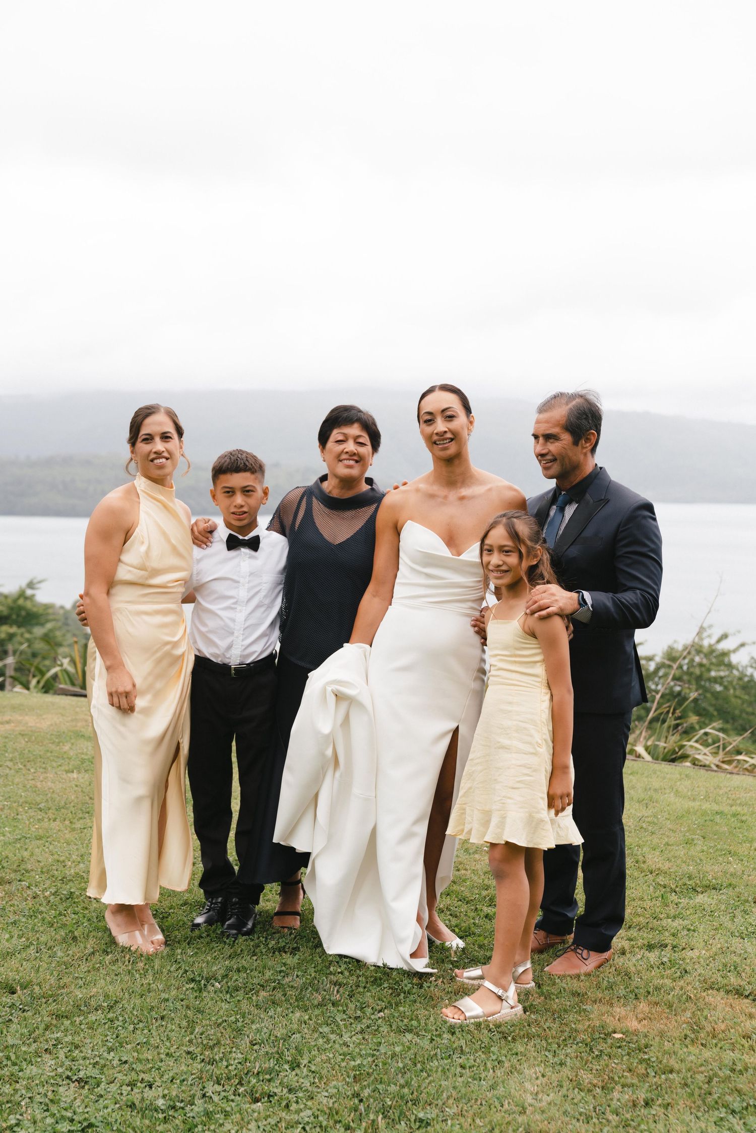 Wedding party group poses together outdoors with a scenic mountain lake backdrop.