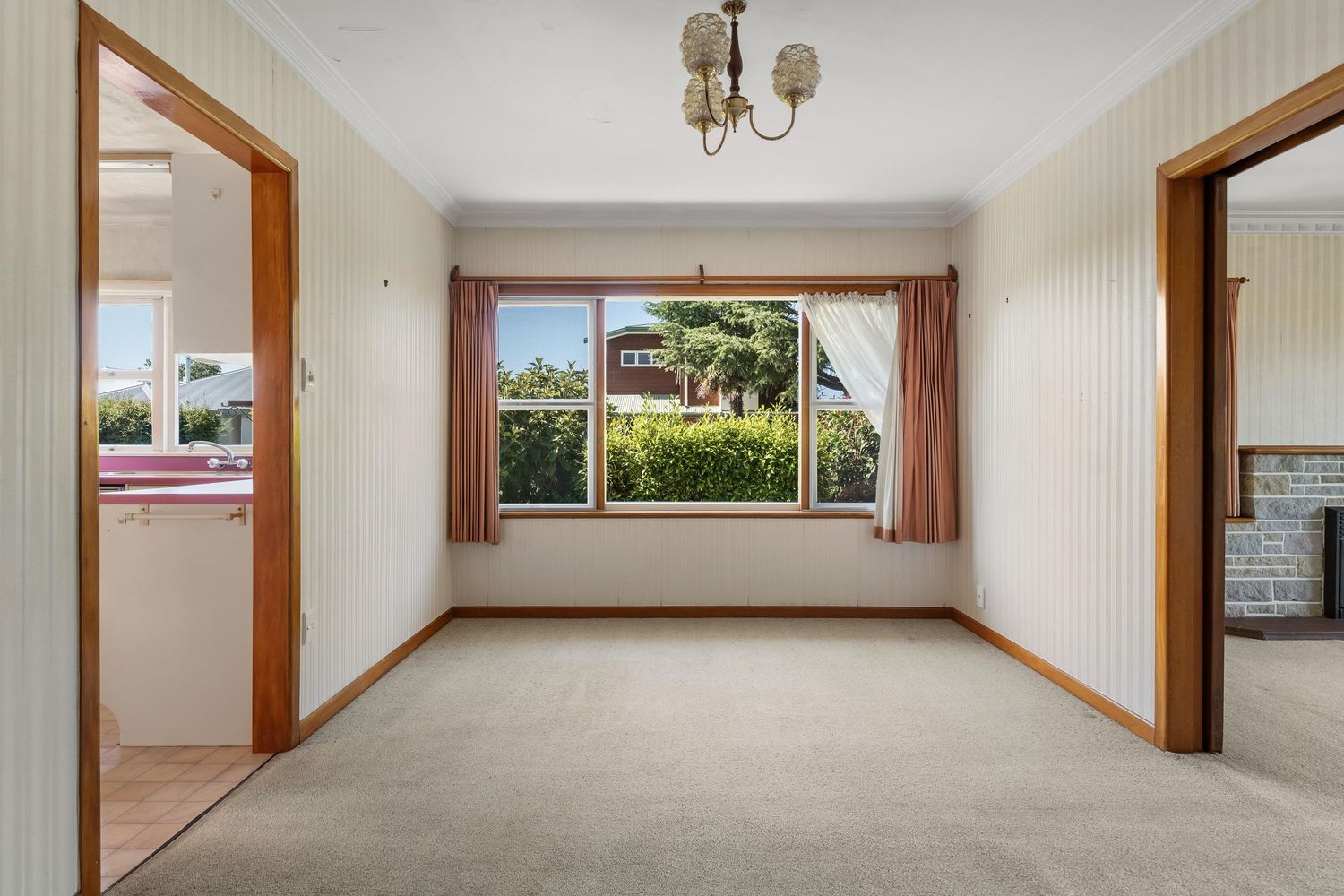 Empty carpeted room with large window and wooden doorframes in neutral tones.