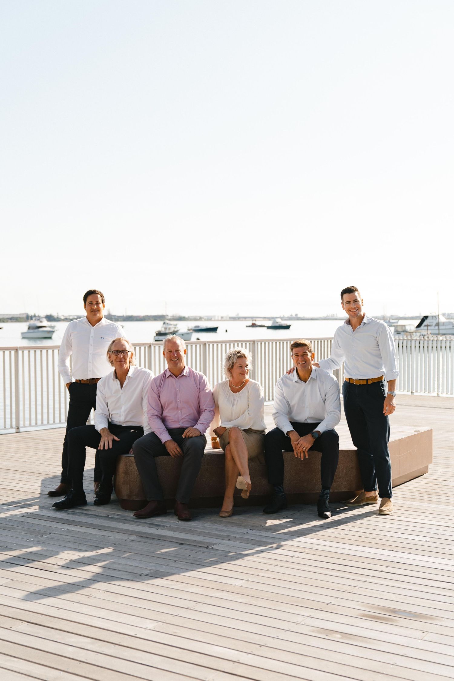 Group of professionals sitting and standing together on a waterfront deck during a sunny day.