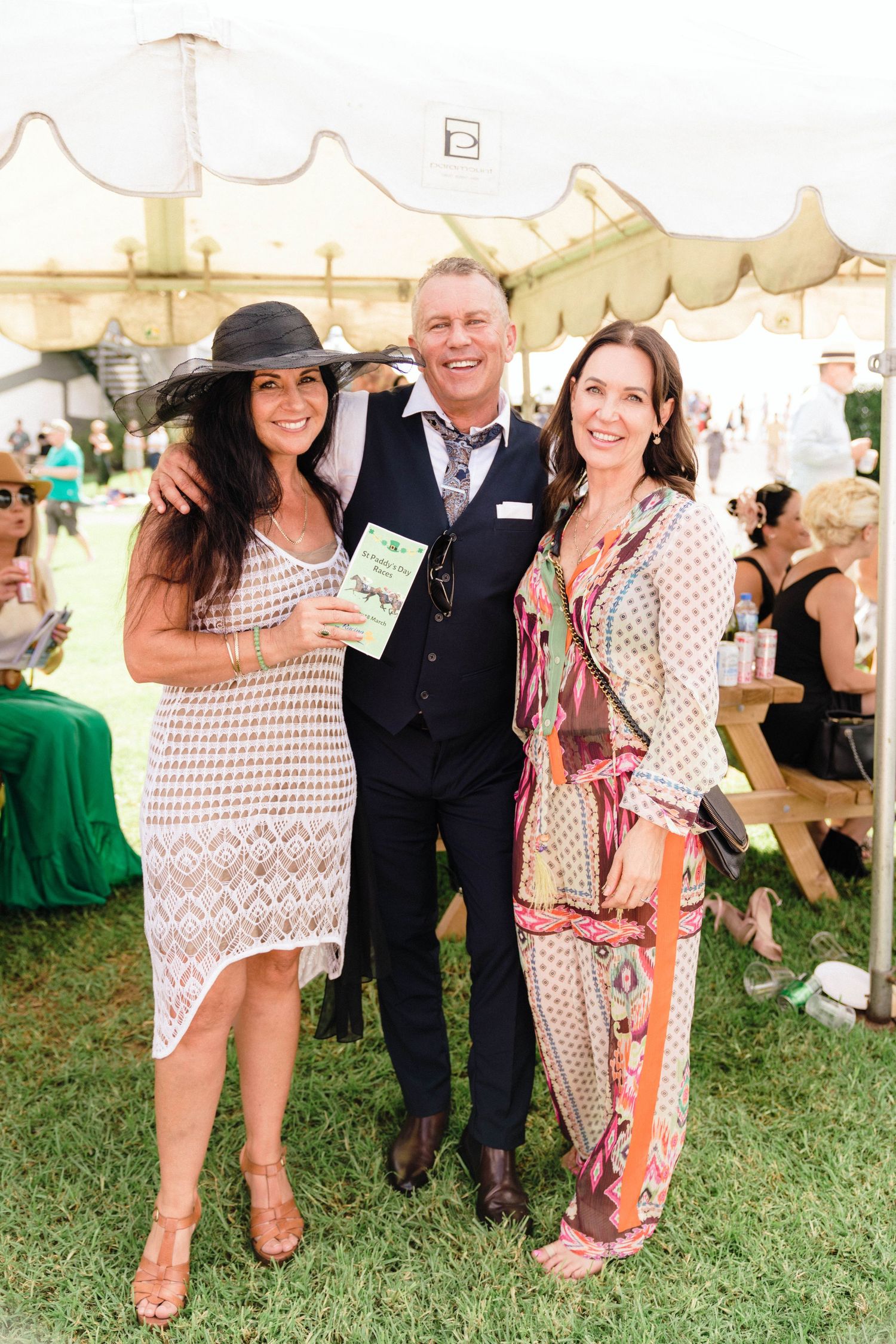 Group in summer attire gathered under a white tent at an outdoor event.