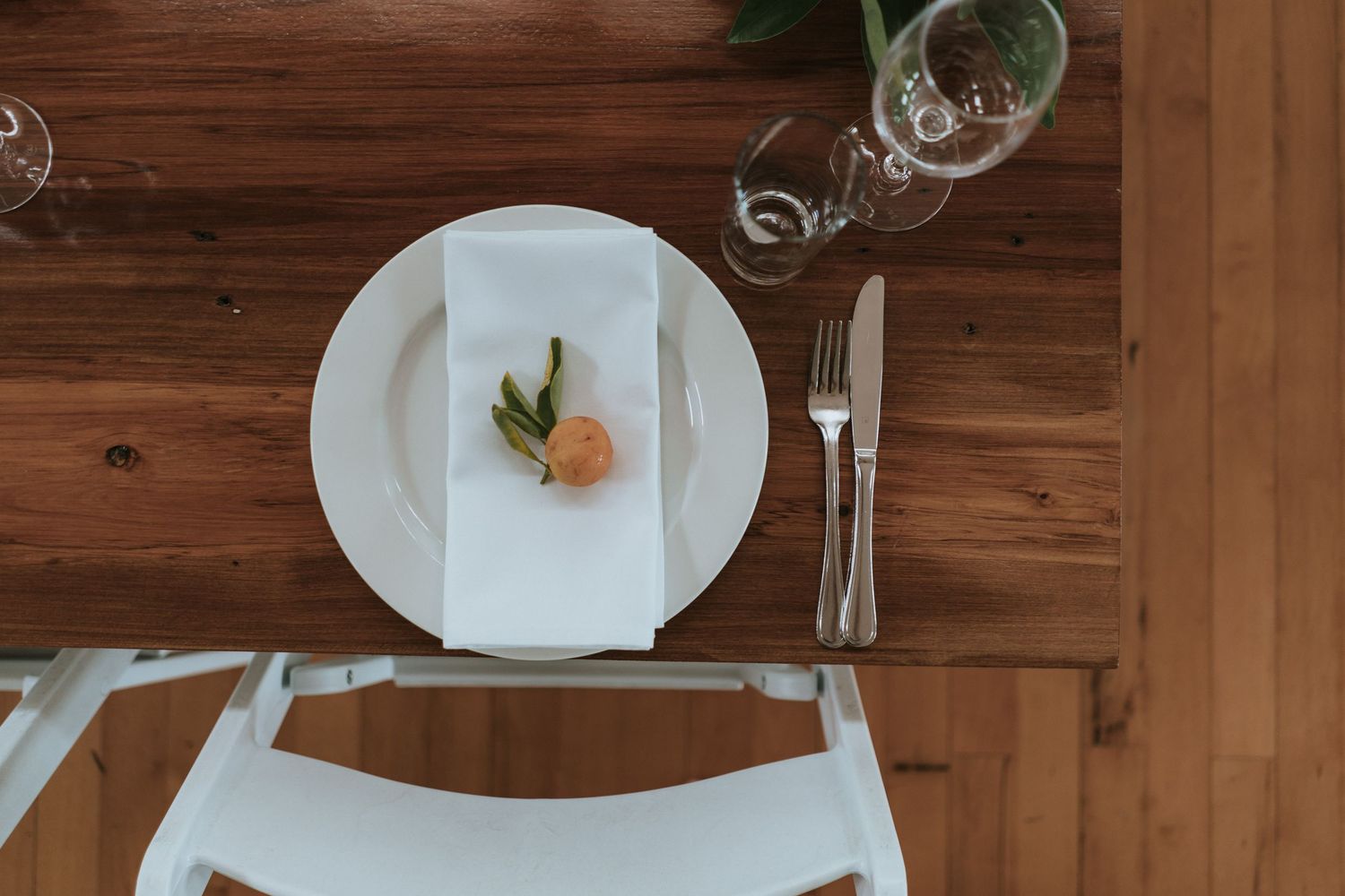 Minimalist table setting with white plate, napkin, and cutlery on rustic wooden surface.