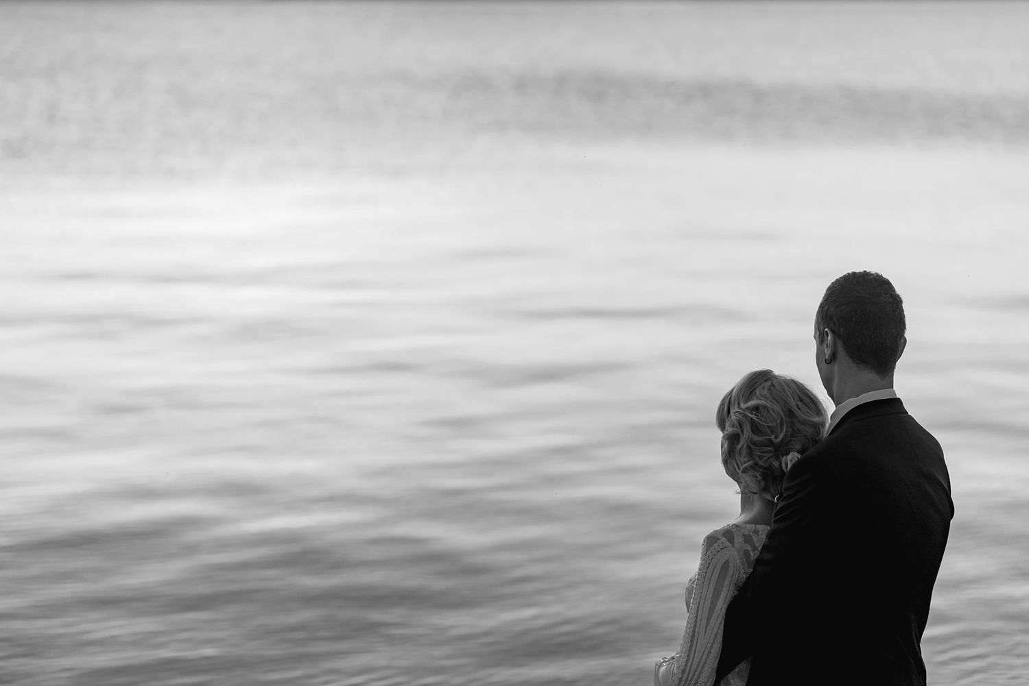 Two silhouettes stand close together against a moody gray ocean backdrop.