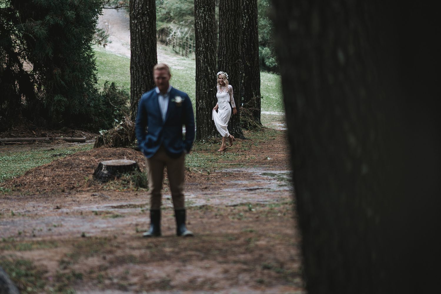 Dark silhouettes of tree trunks in a misty forest setting with figures walking in the distance.
