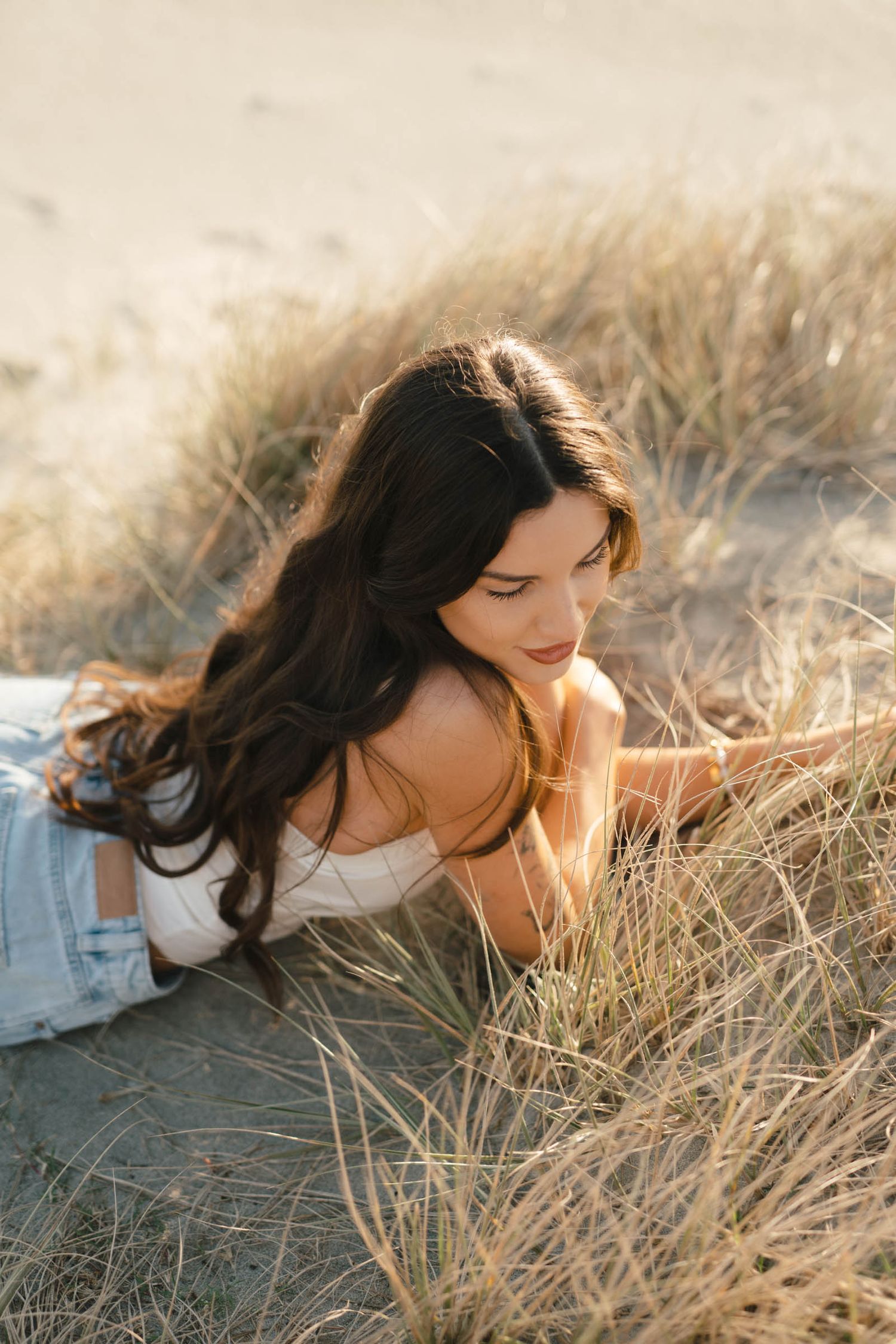 Dreamy portrait in beach grass wearing white top with flowing dark hair.