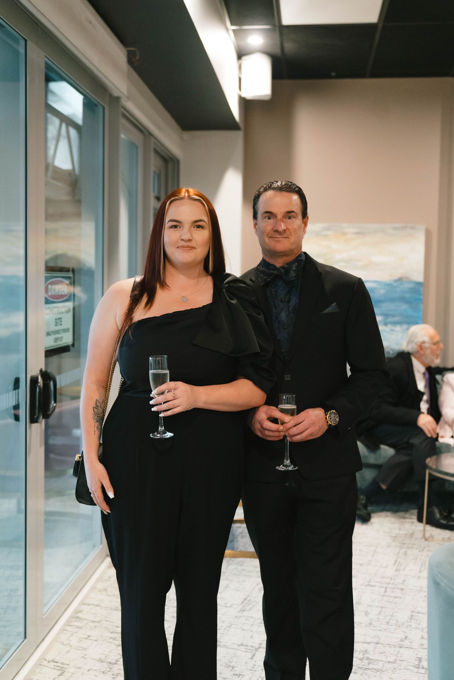 Couple in formal black attire holding champagne glasses at an event.