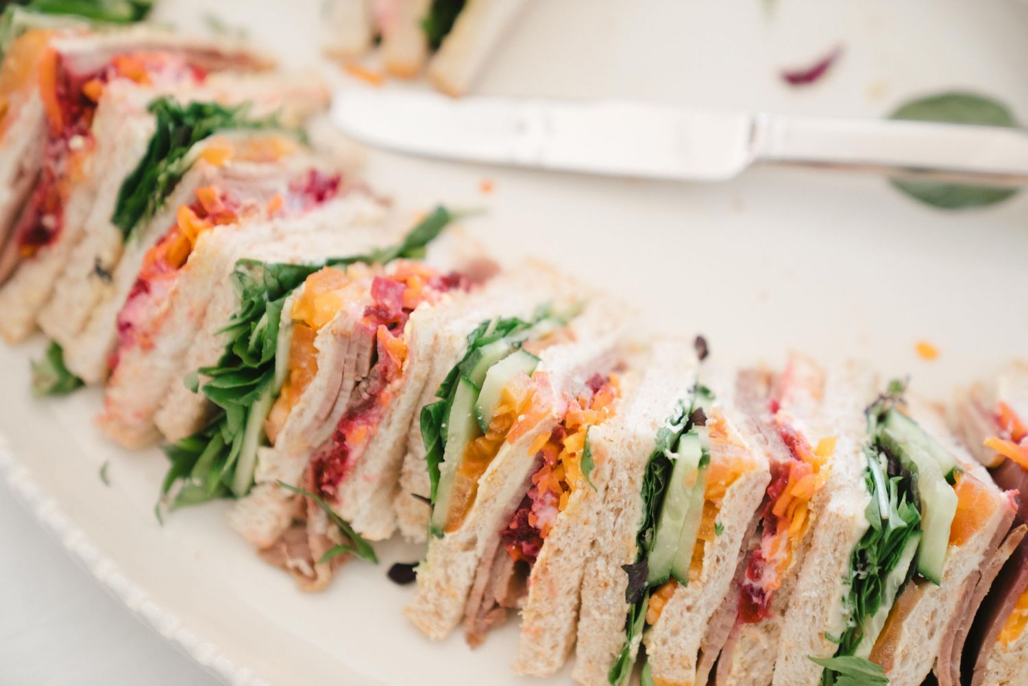 Club sandwich slices arranged on white plate with layers of turkey, lettuce, tomato and bacon between toasted bread.