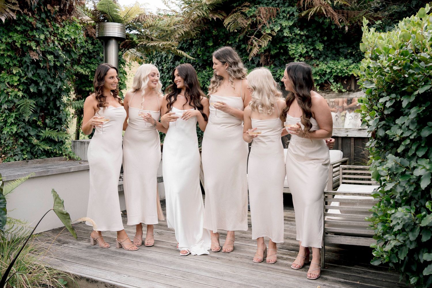A row of figures in elegant white dresses stand together on garden steps during a wedding celebration.