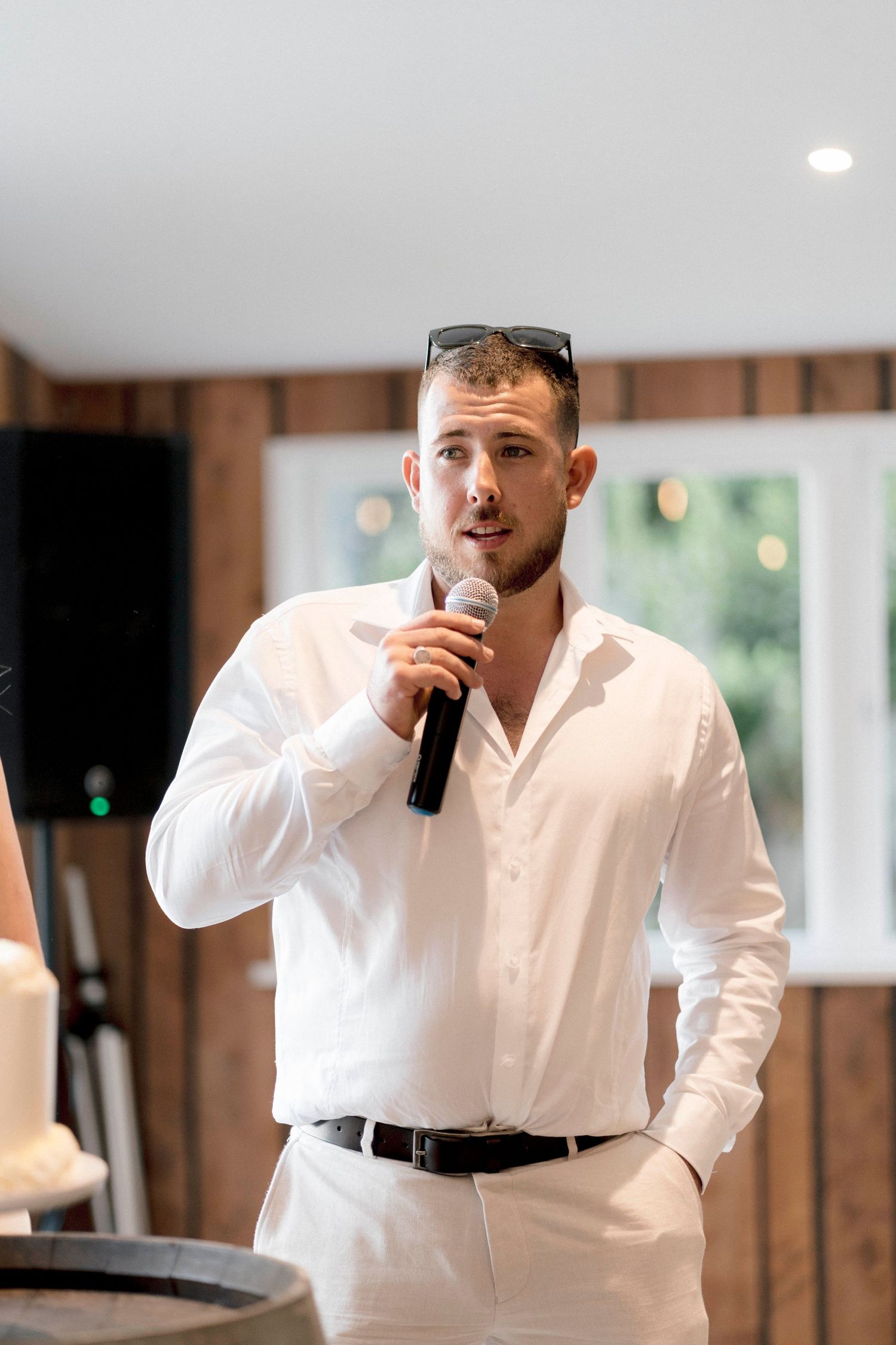A person in a white shirt giving a speech with a microphone at an indoor wedding reception venue.