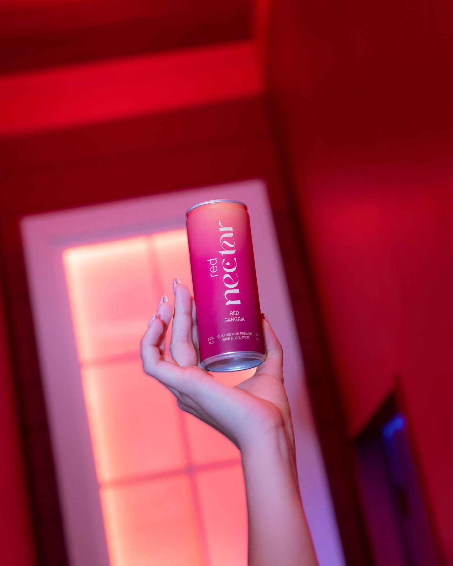 A hand holding a pink Nectar can against a red illuminated background.