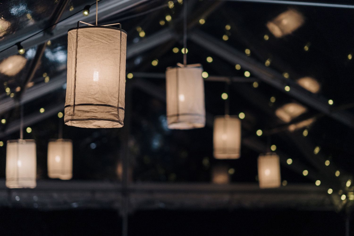 Paper lanterns illuminated at night against a dark ceiling decorated with twinkling string lights.