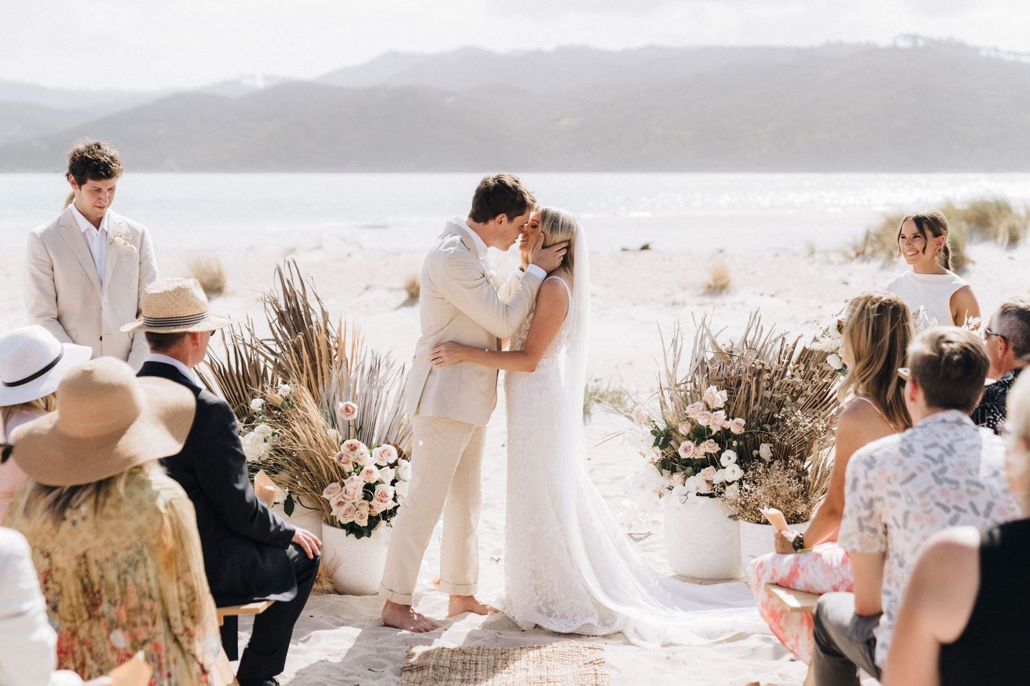 Beachside ceremony with natural decor and floral arrangements on a sunny day.