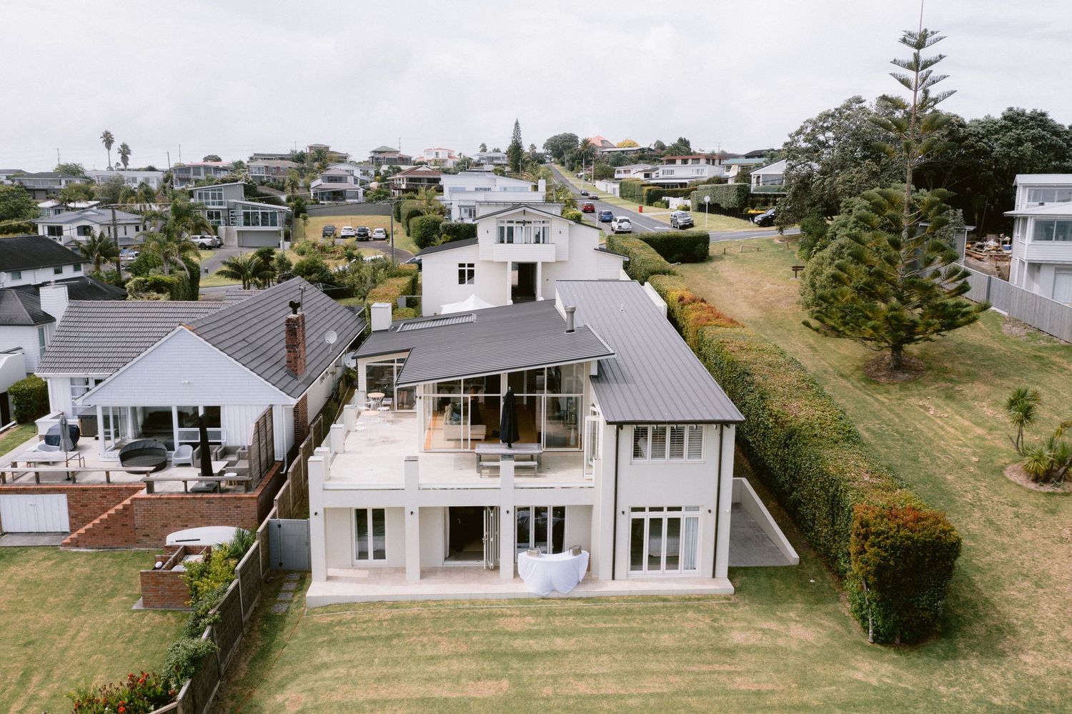 Aerial panoramic view of coastal residential homes along a beachfront community with lush green lawns.